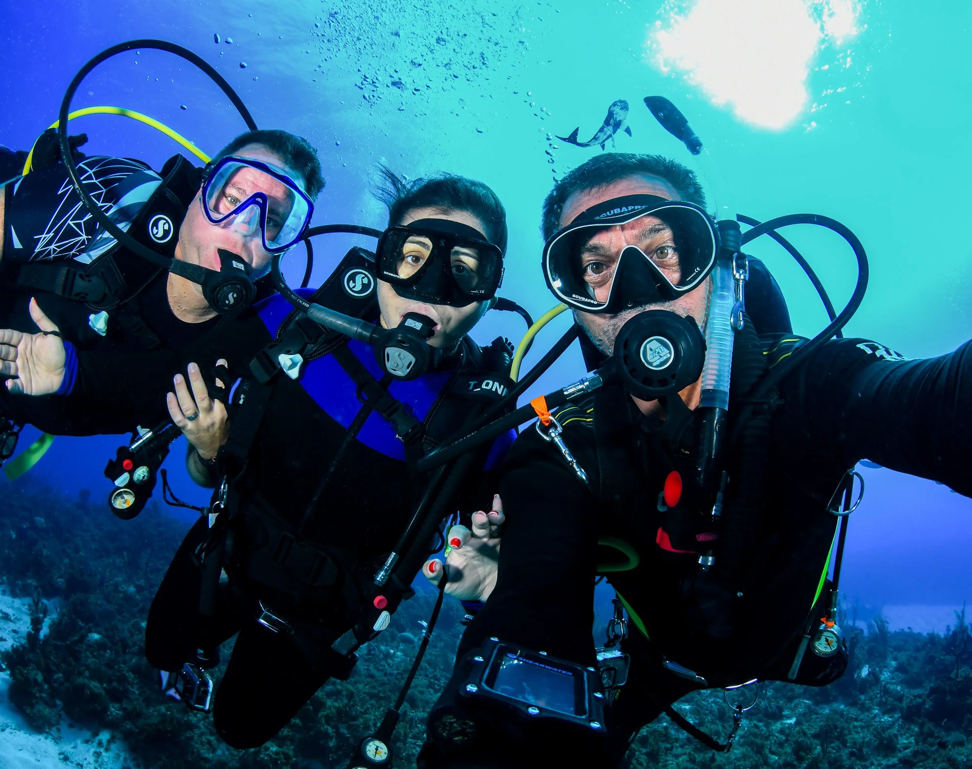 Three scuba divers posing together above a coral reef in Jamaica.