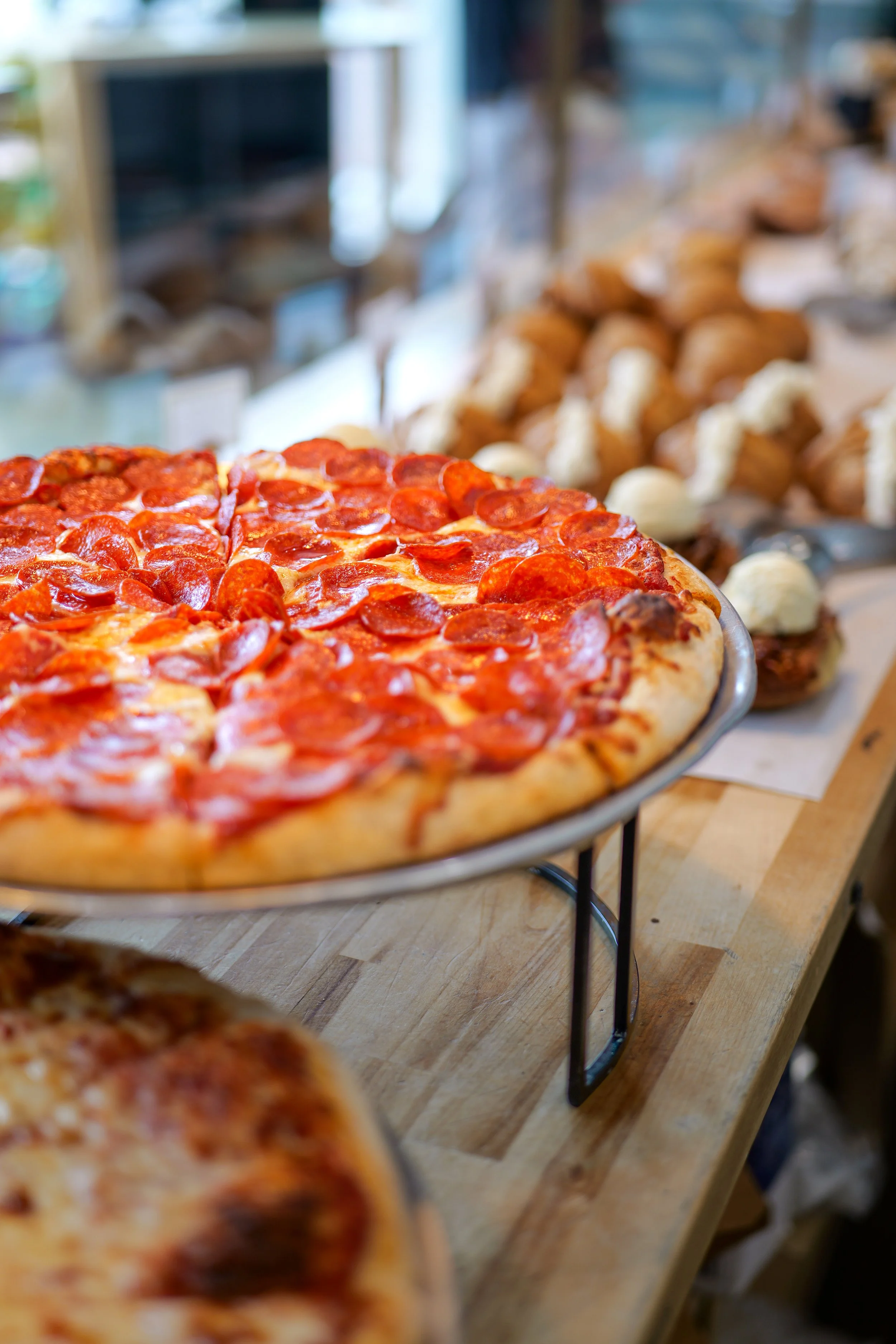 Pepperoni pizza displayed on a stand on a wooden table in a pizzeria.