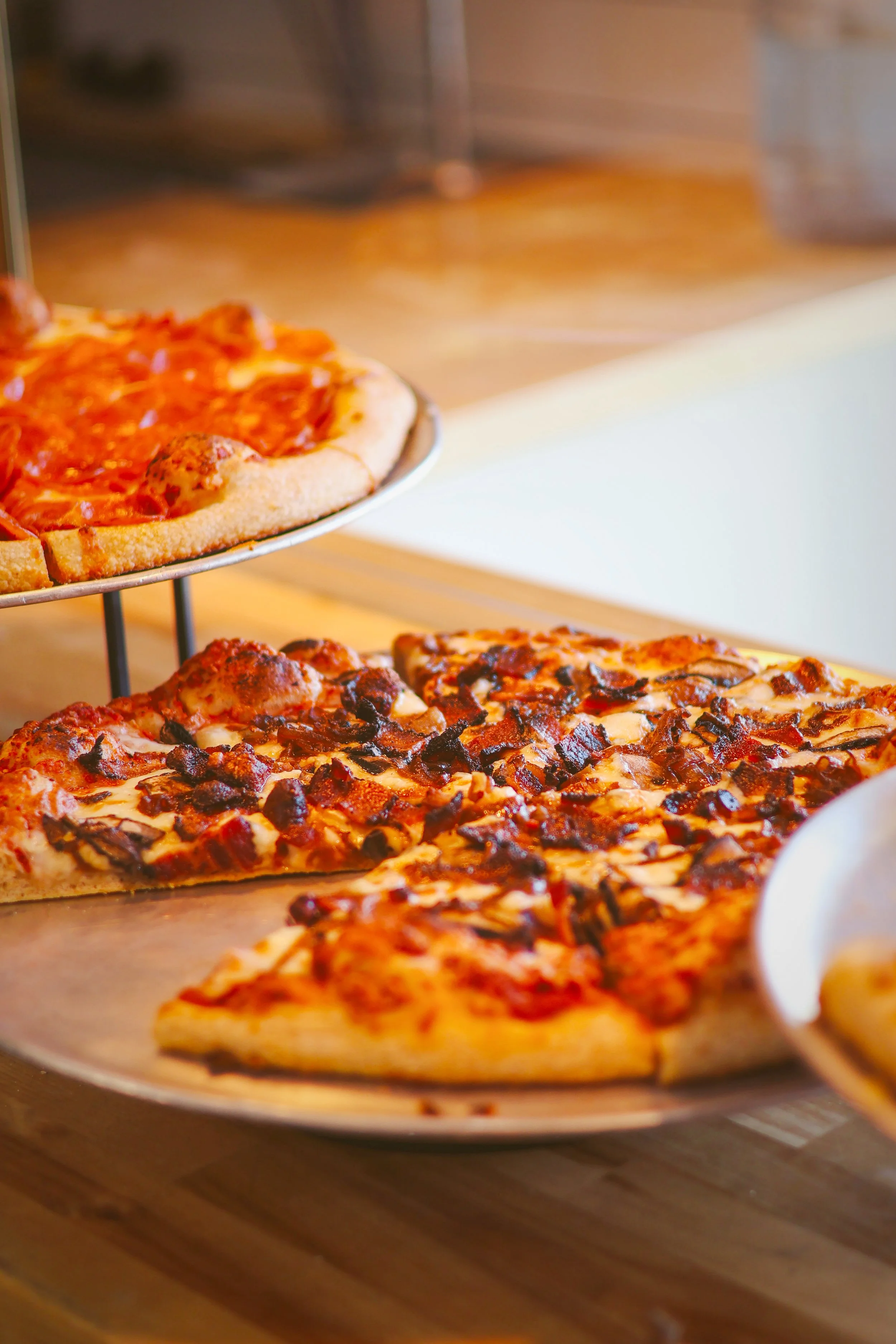 Three pizzas on a display tray, two with cheese and toppings and one simple cheese pizza, on a wooden surface.