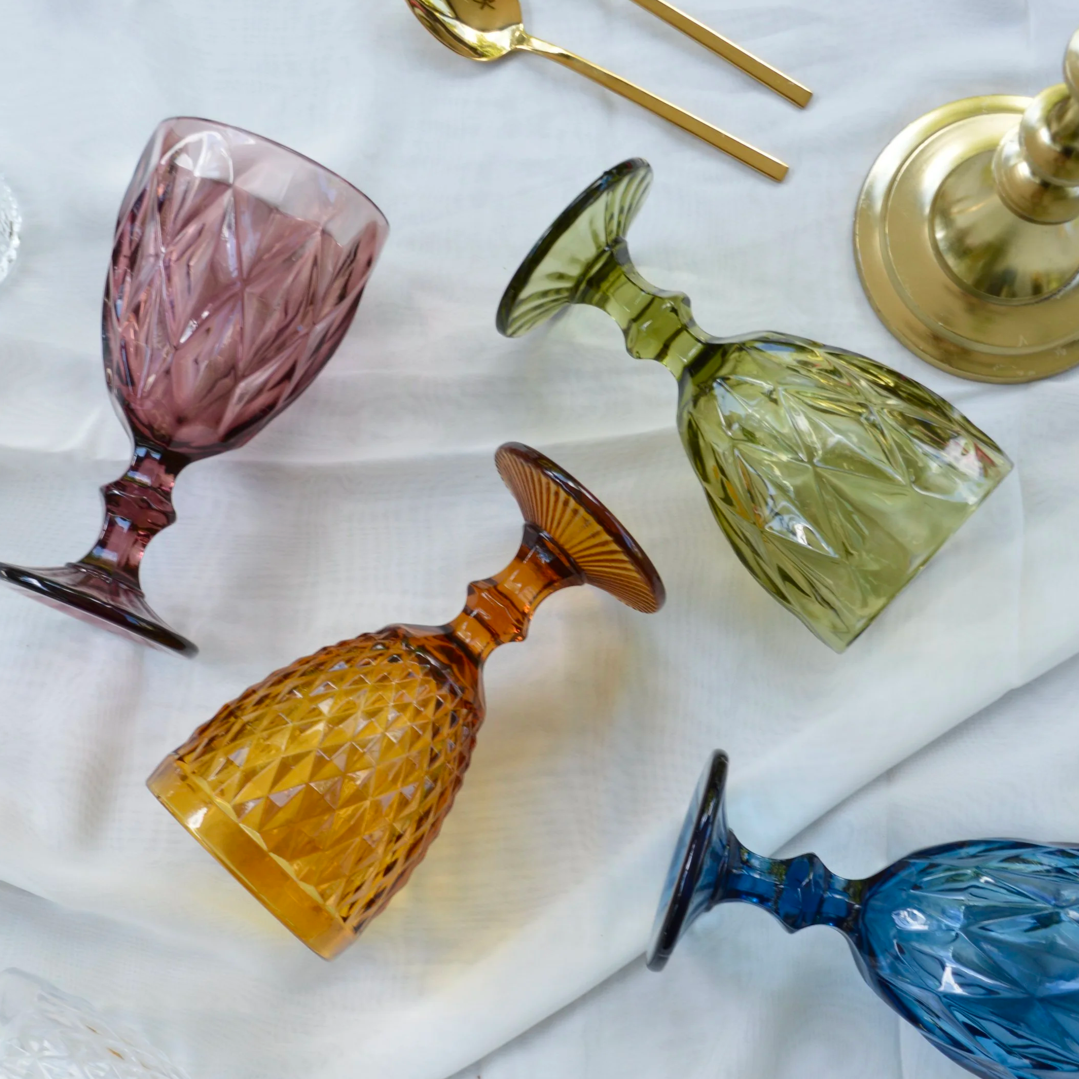 Colorful cut glassware including pink, yellow, green, blue, and amber glasses displayed on a white surface.