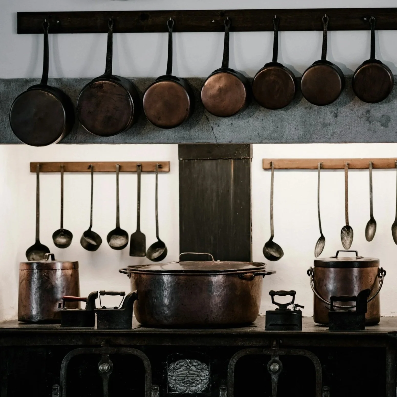 Vintage kitchen with hanging pots, pans, and utensils, and old-fashioned cooking pots on a stove.