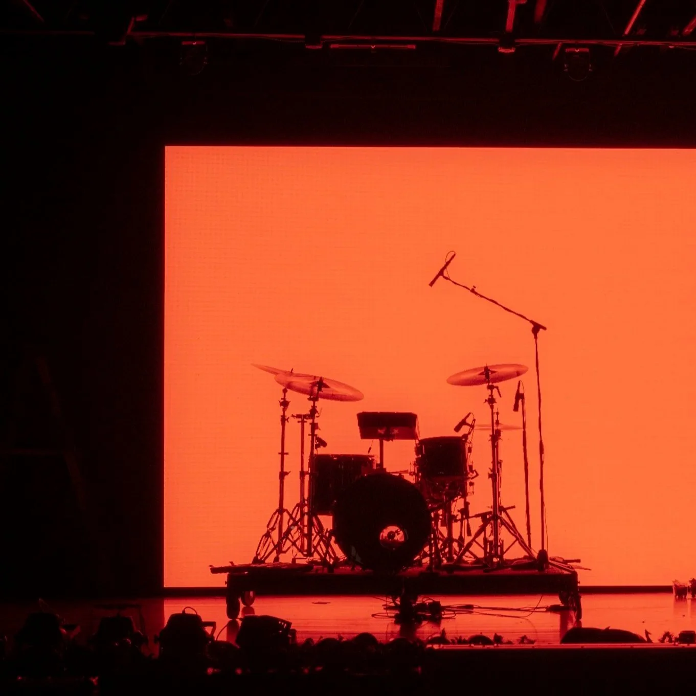 Silhouette of a drum set with a microphone and stand on a stage against an orange background.
