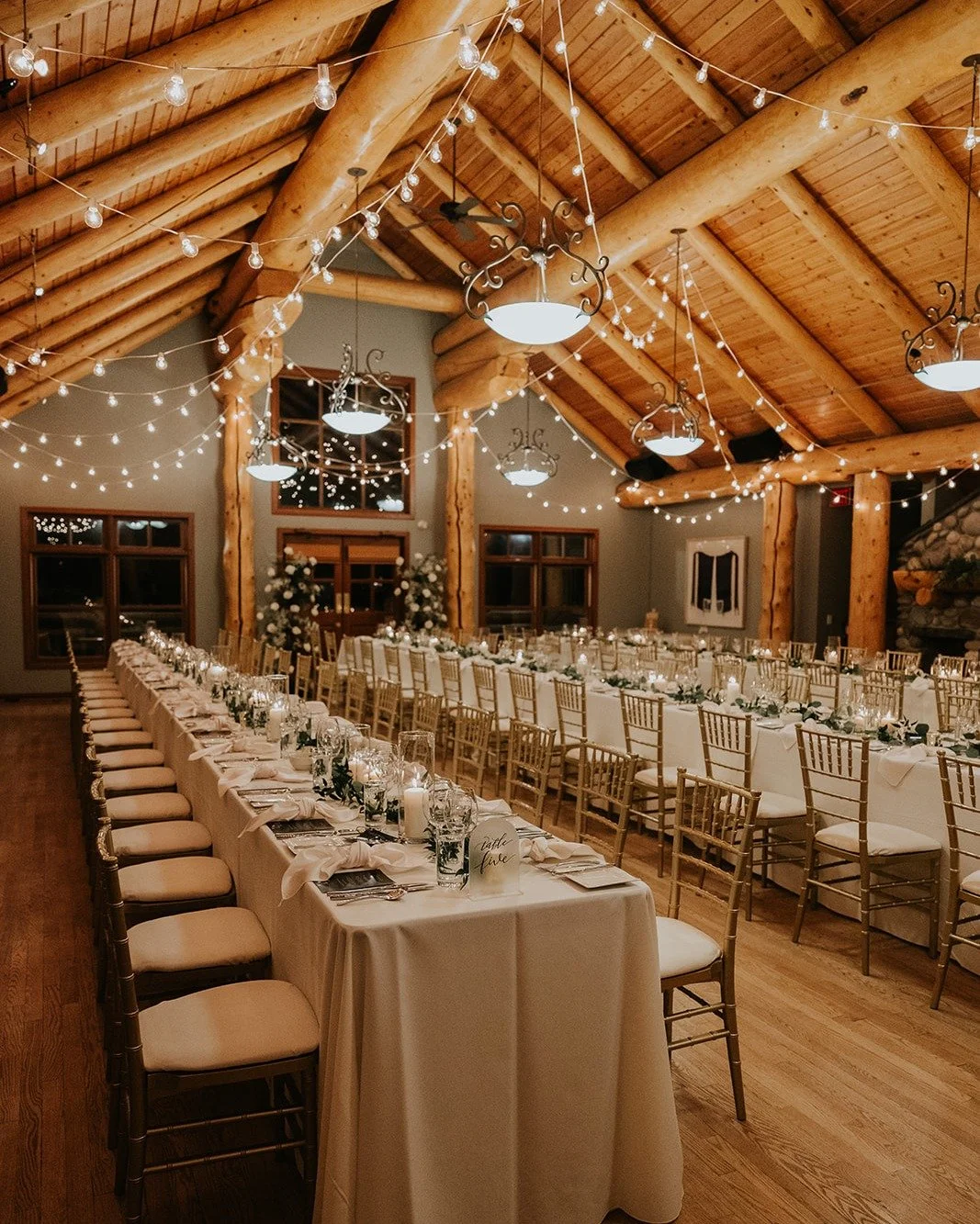 A room like this does the work for you. The soaring timber beams, warm wood tones, and layers of soft lighting create a setting that already feels inviting. From there, simple tables, greenery, and candlelight keep the focus on what matters most: bri