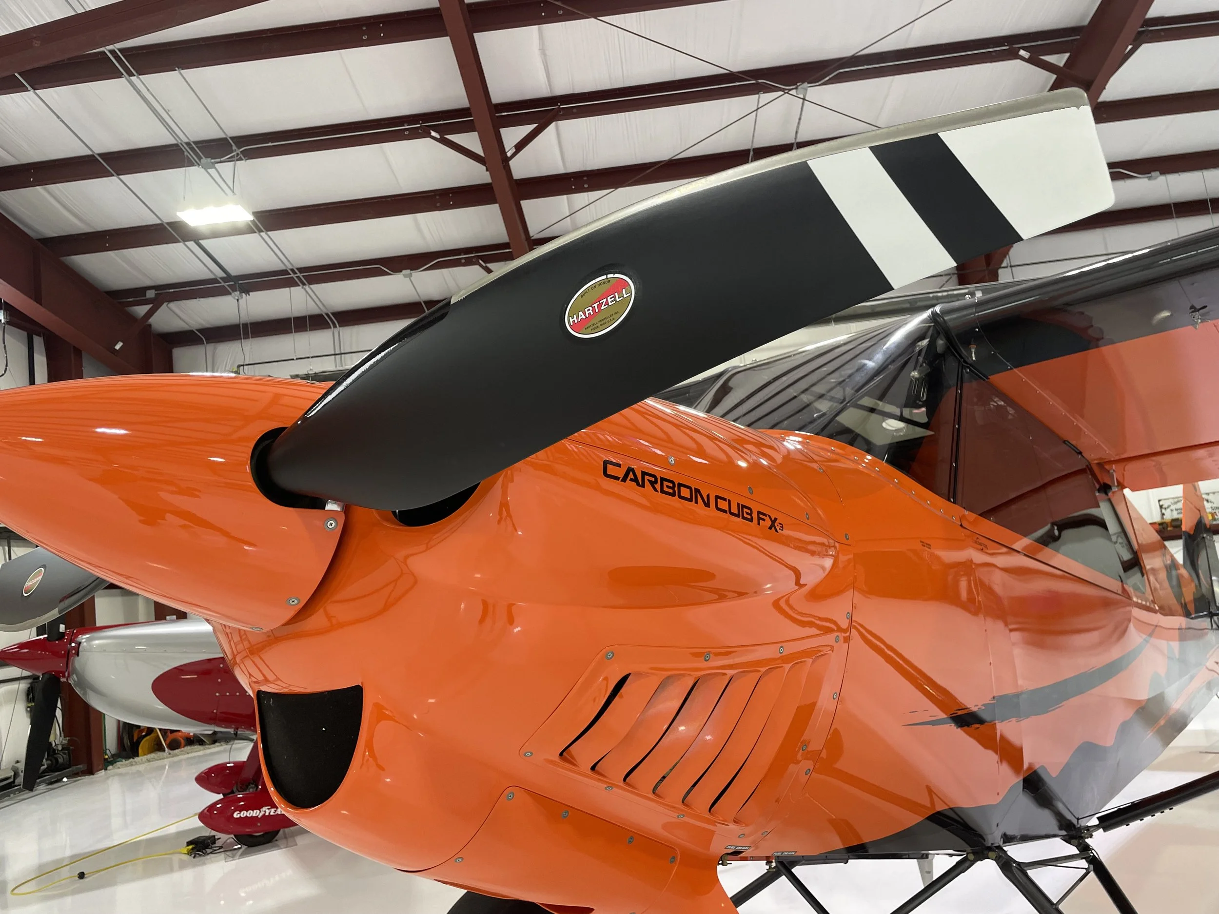 An orange and black Cub Crafters Carbon Cub FX3 in a private hangar.