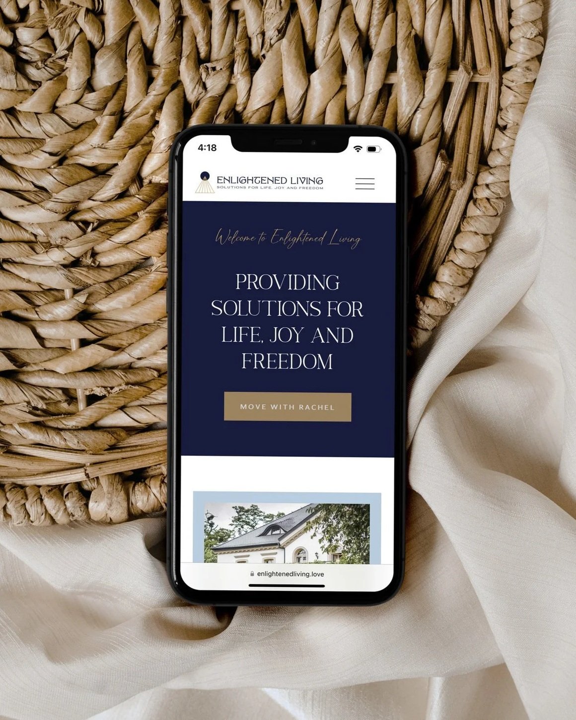 Smartphone displaying the homepage of Enlightened Living website, with a dark blue background, white text, and a beige button, placed on a woven basket with white fabric.
