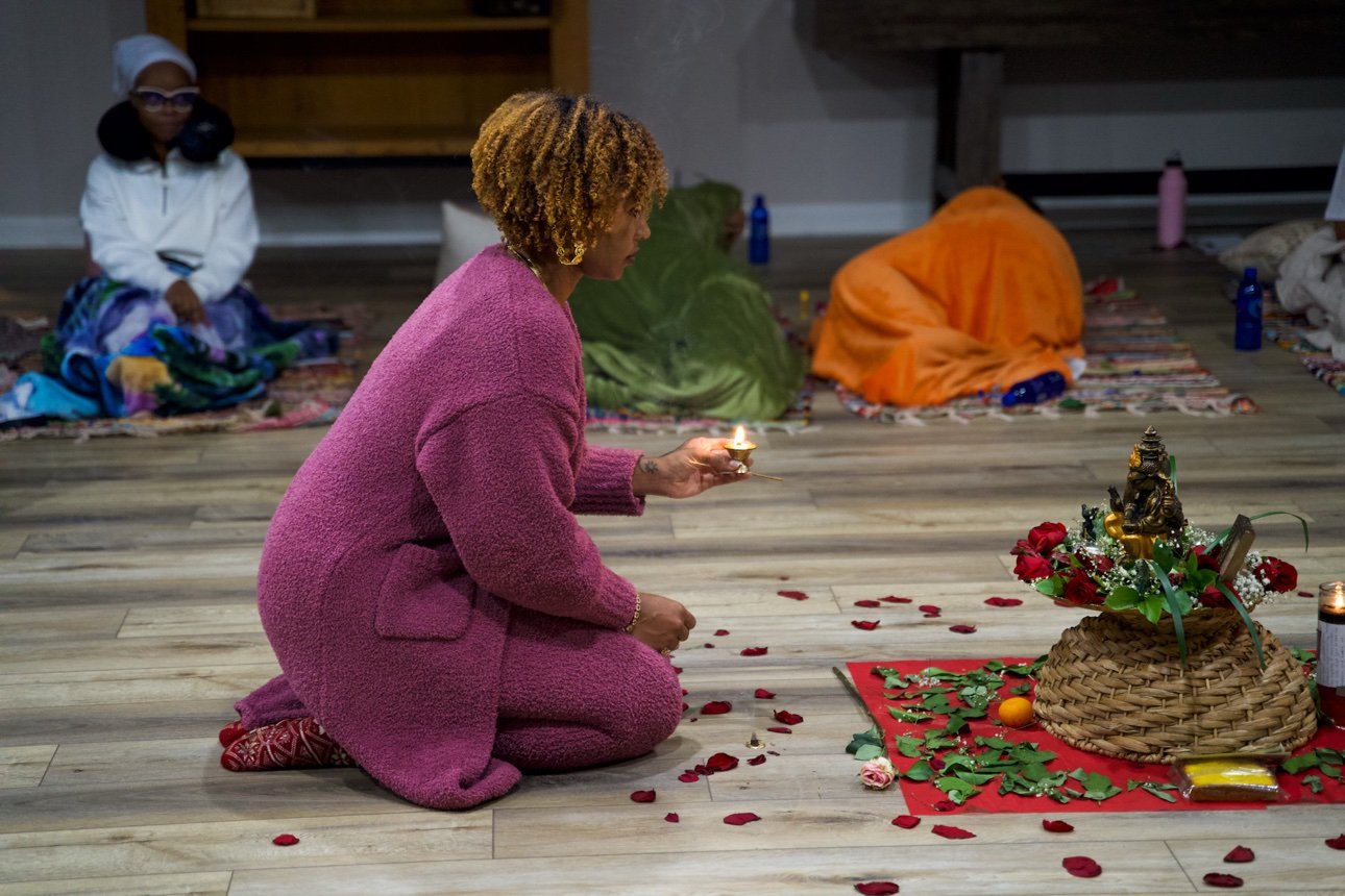 Ashley kneeling with a lit candle before the flower altar — her photograph.