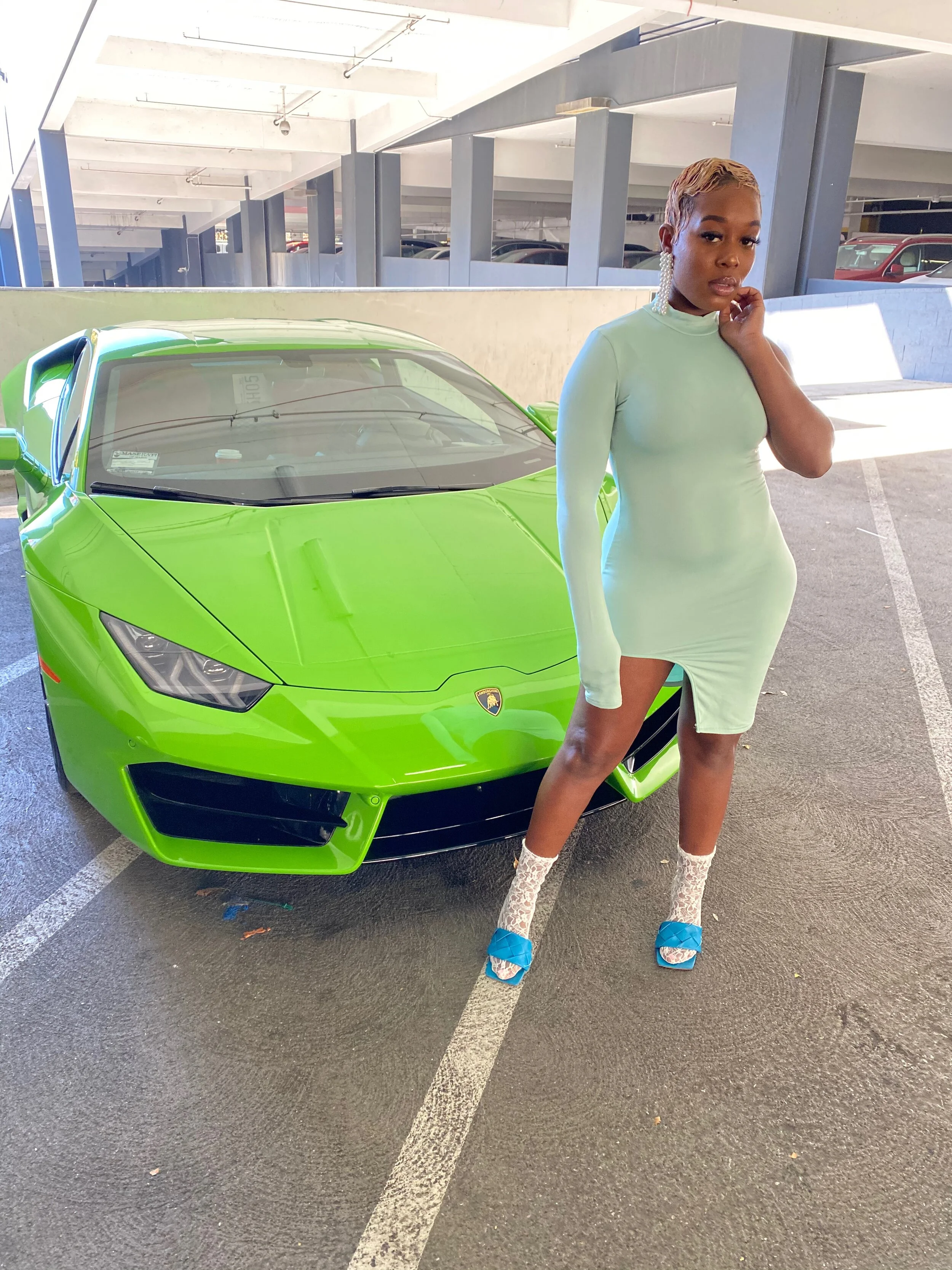 A woman in a light green dress standing next to a bright green luxury sports car in a parking garage.
