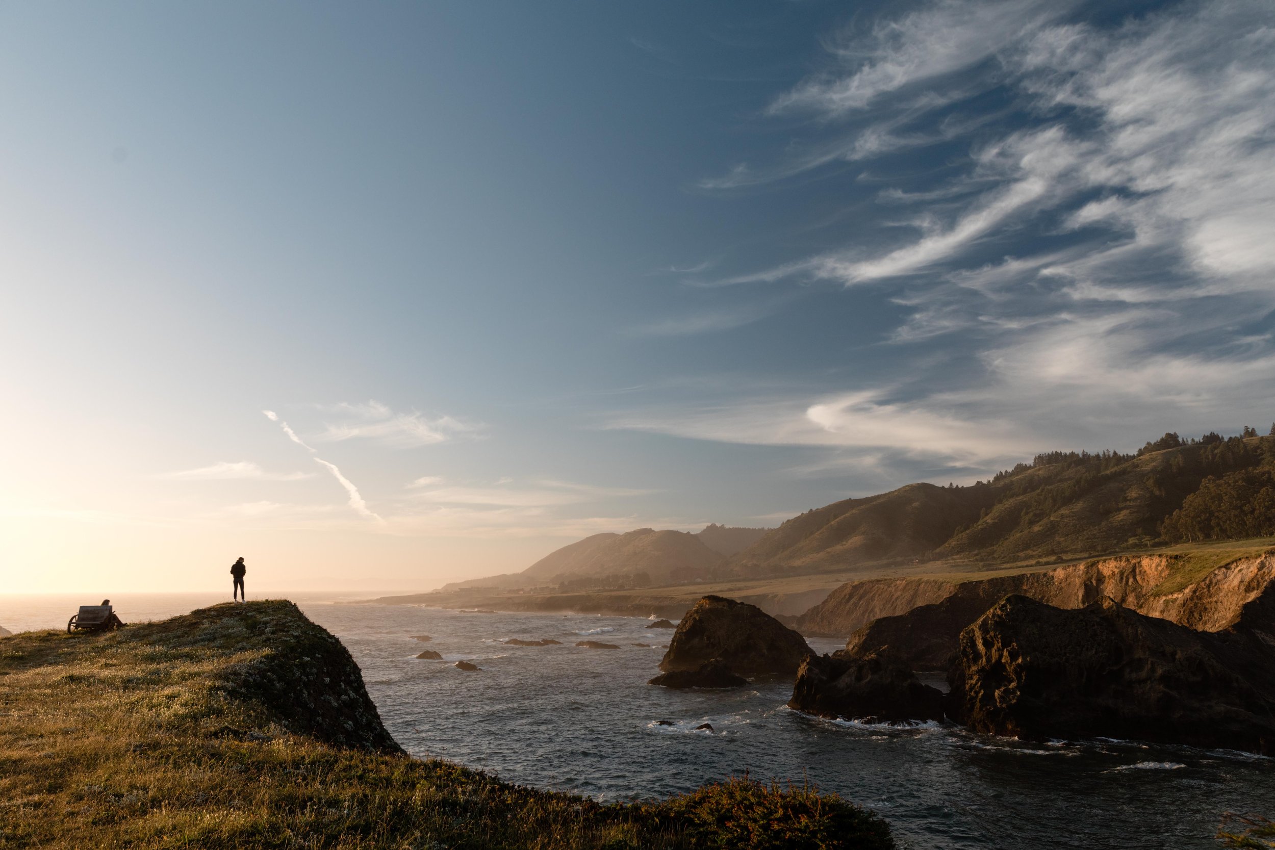 Panoramic view of rocky Pacific Coastline with a man's silhouette standing on the edge