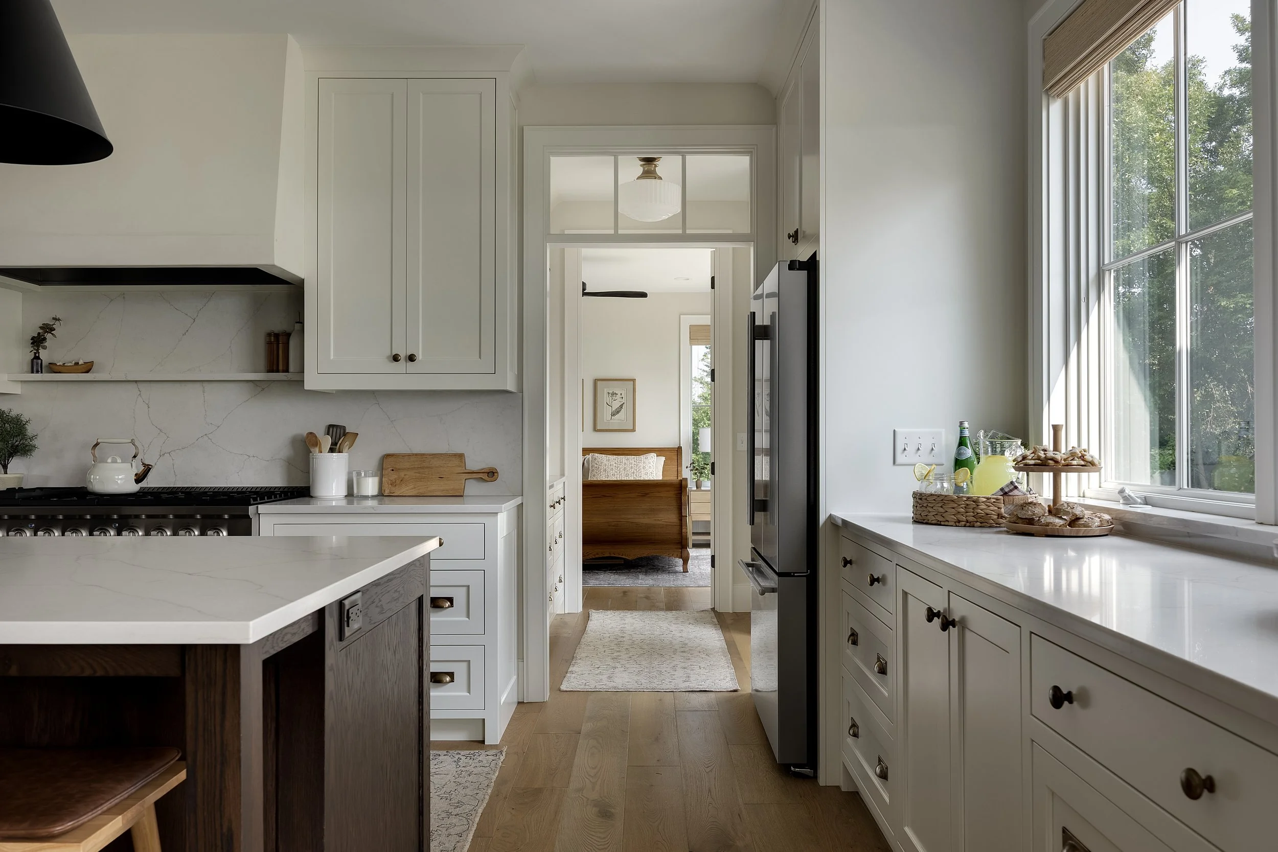Bright kitchen with white cabinets, a window with a view of trees, and a glimpse into a dining room with a wooden bench.