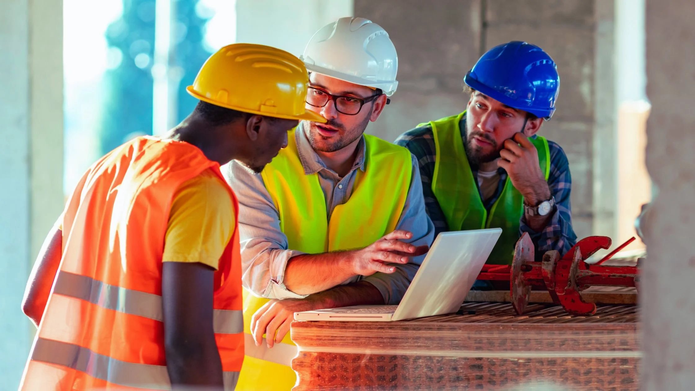 Construction workers wearing safety helmets and high-visibility vests reviewing their website progress on a laptop at a building site in Perth.