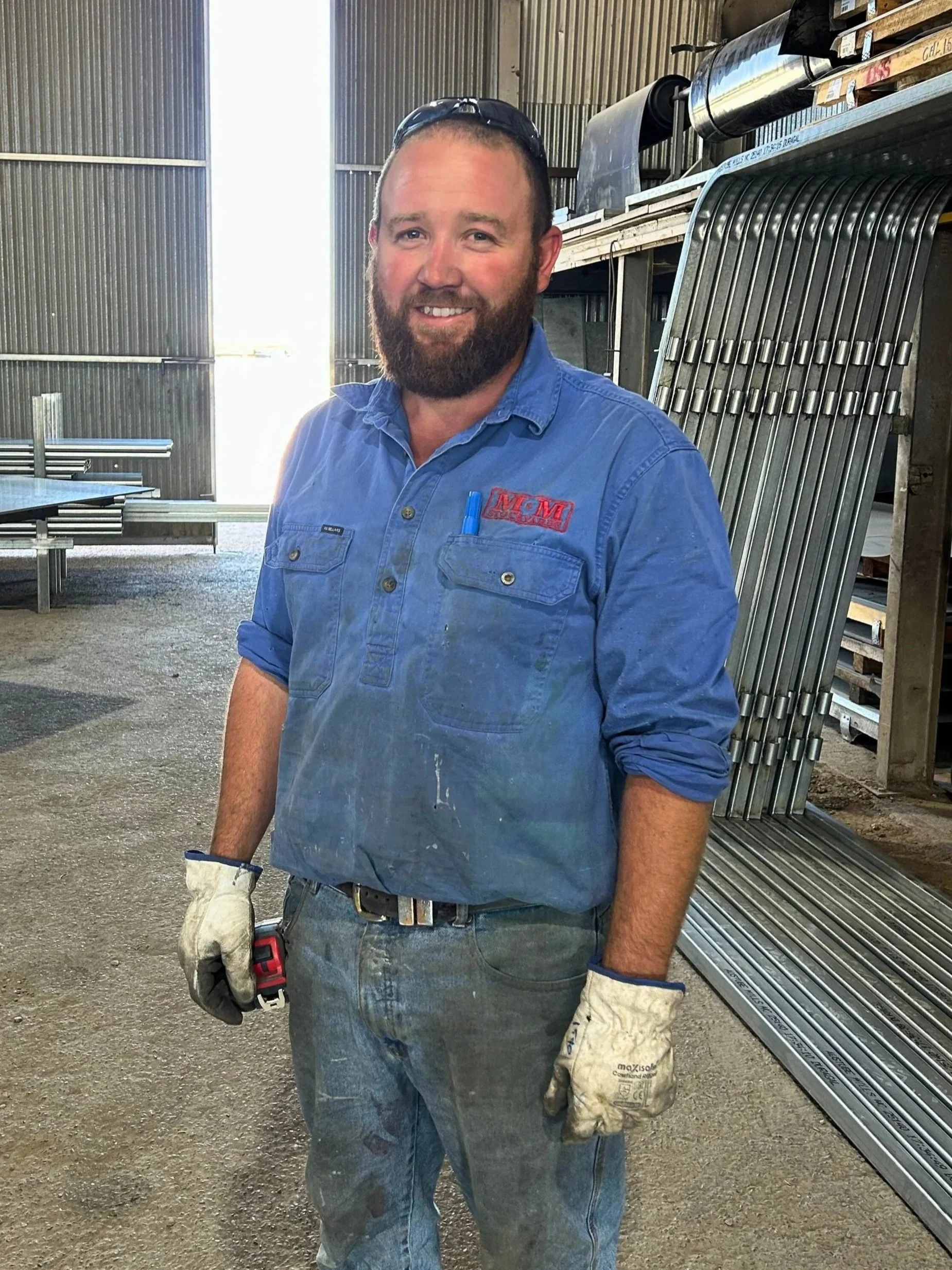 A man with a beard wearing a blue checkered shirt with logos, standing in a barn.