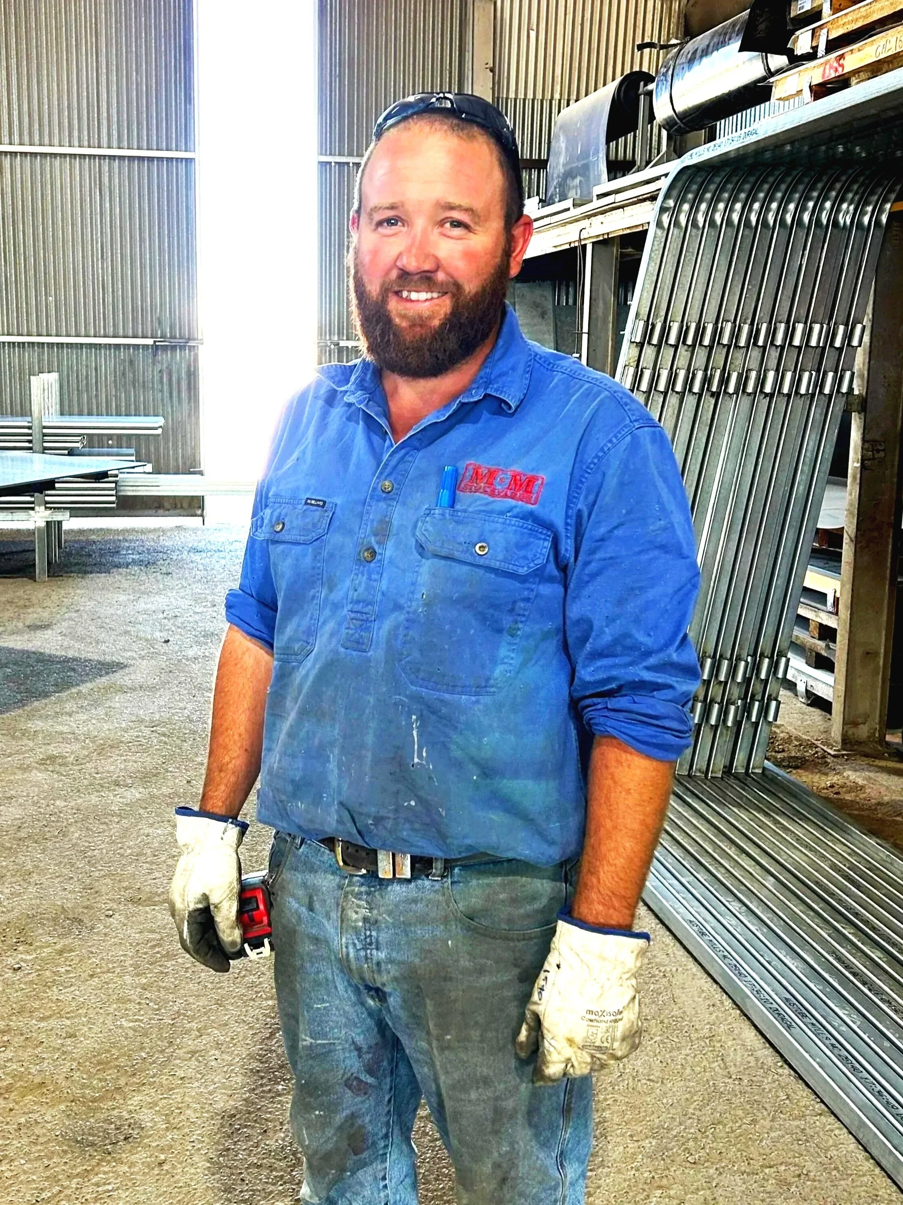 A man with a beard wearing a blue checkered shirt with logos, standing in a barn.