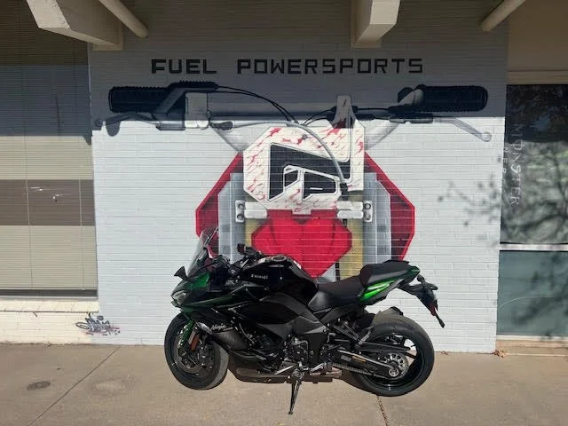 Black motorcycle parked in front of a white brick wall with a large Fuel Powersports logo and a red heart symbol.