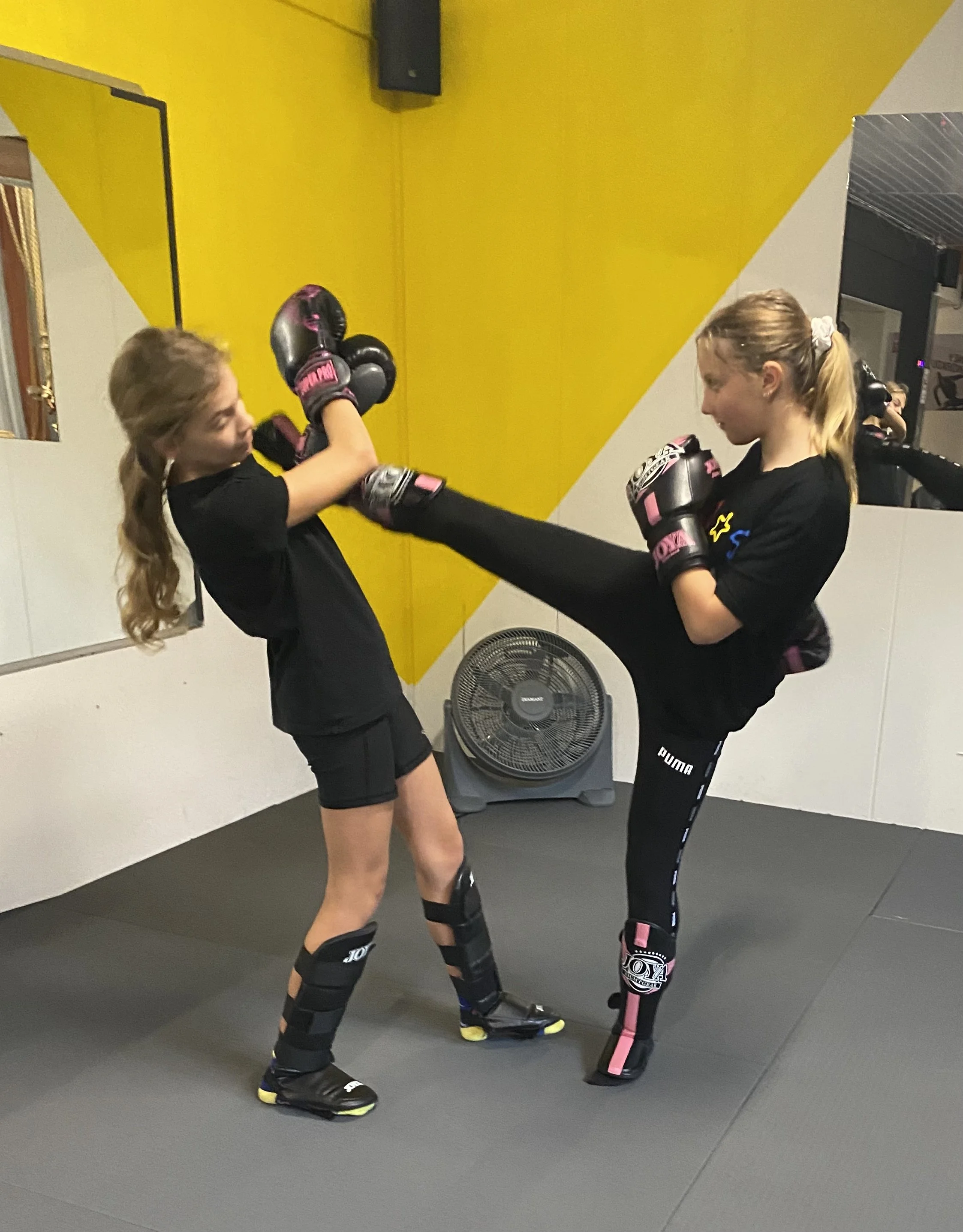 Binnenruimte van een fitness- of martial artschool met veel mensen die oefenen met bokshandschoenen en focus pads, gekleed in sportkleding.