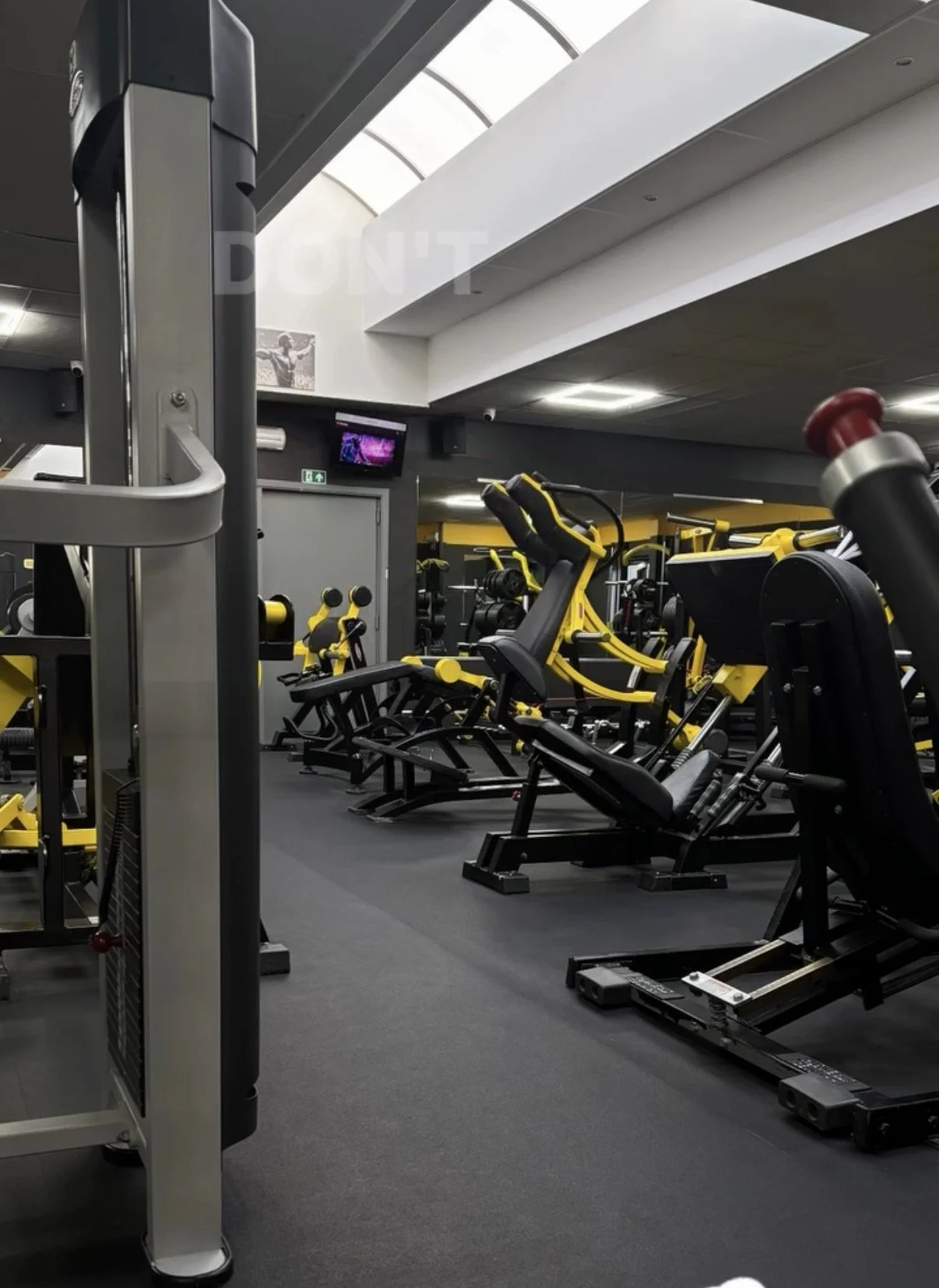 Fitnessruimte met diverse trainingsapparaten, waaronder cardiomachines en gewichten, in een sportschool met hoge ramen en plafond.