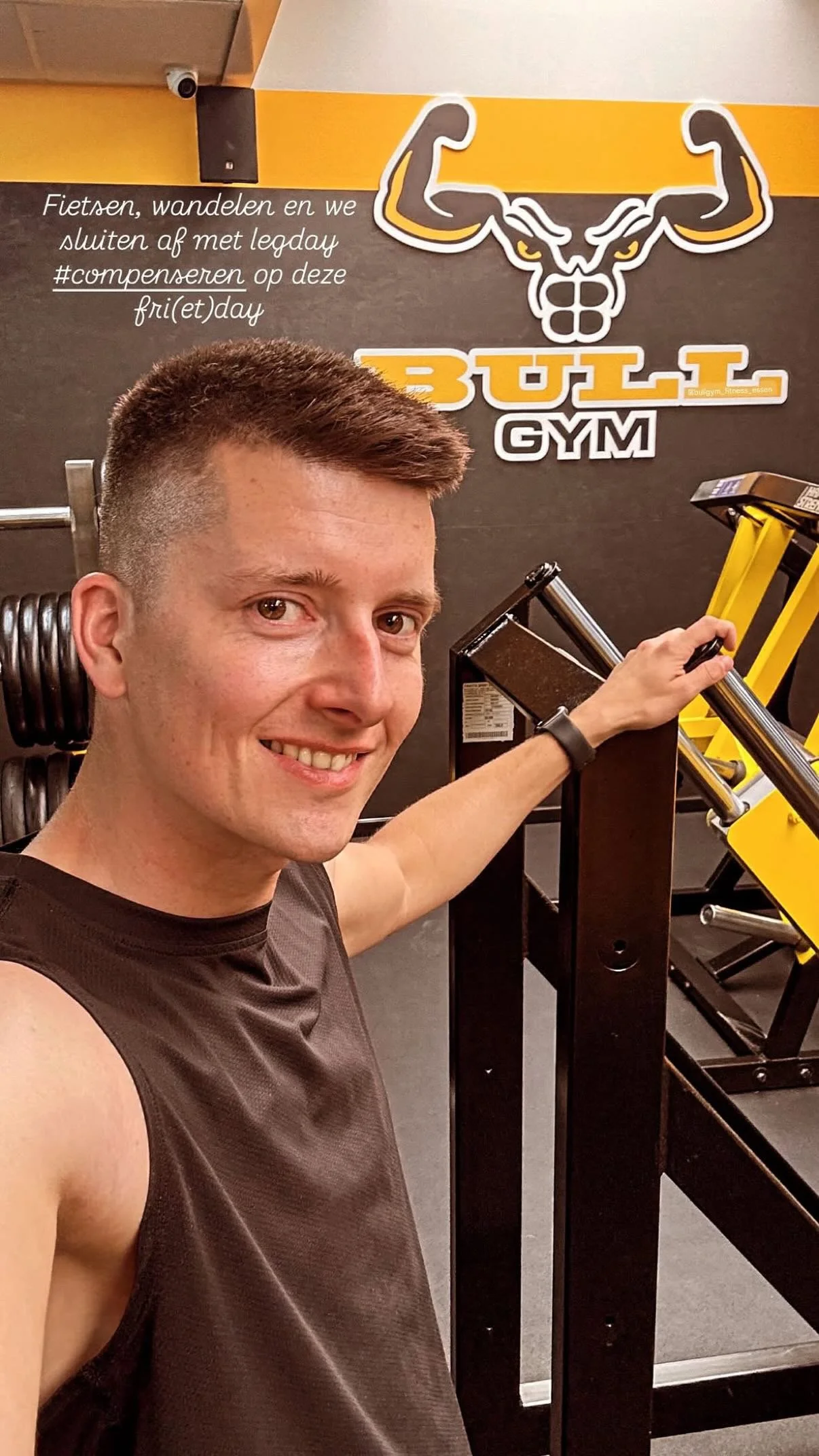 Man die in een fitnessruimte staat, met een grote spierachtige bokkenkop en de tekst 'BULL GYM' op de muur achter hem.
