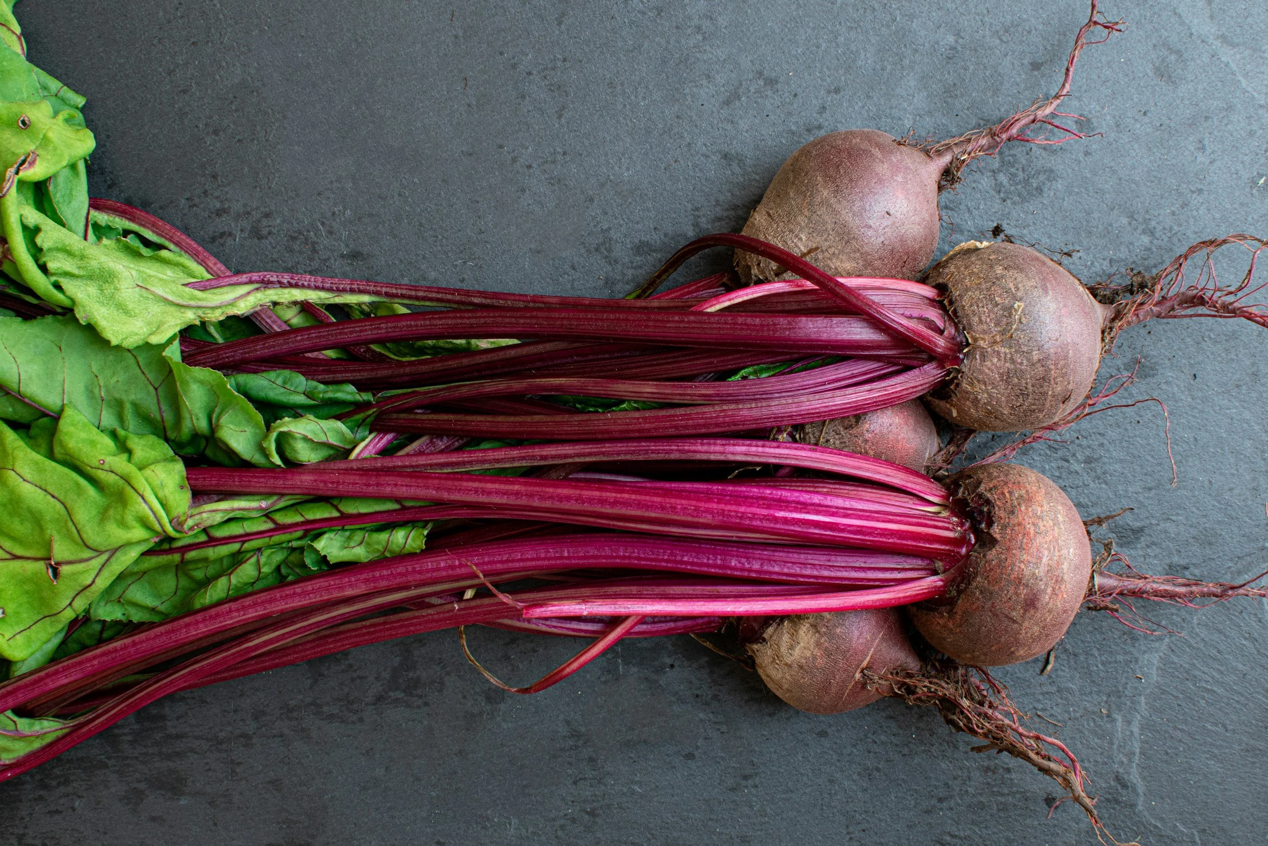 beet vegetables lying on a gray table with greens still attached