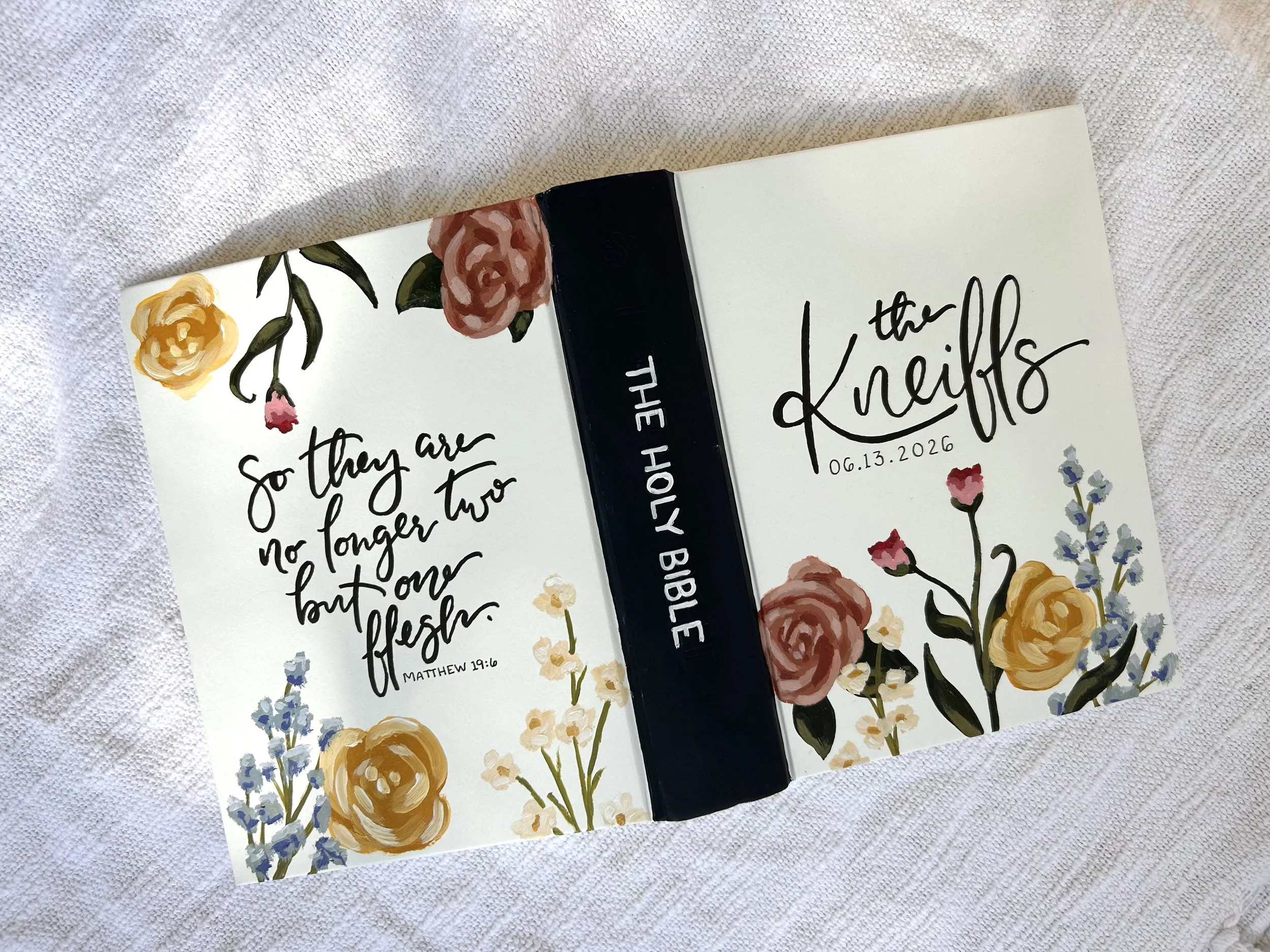 Close-up of an open book with floral illustrations and handwritten text on a white textured surface.
