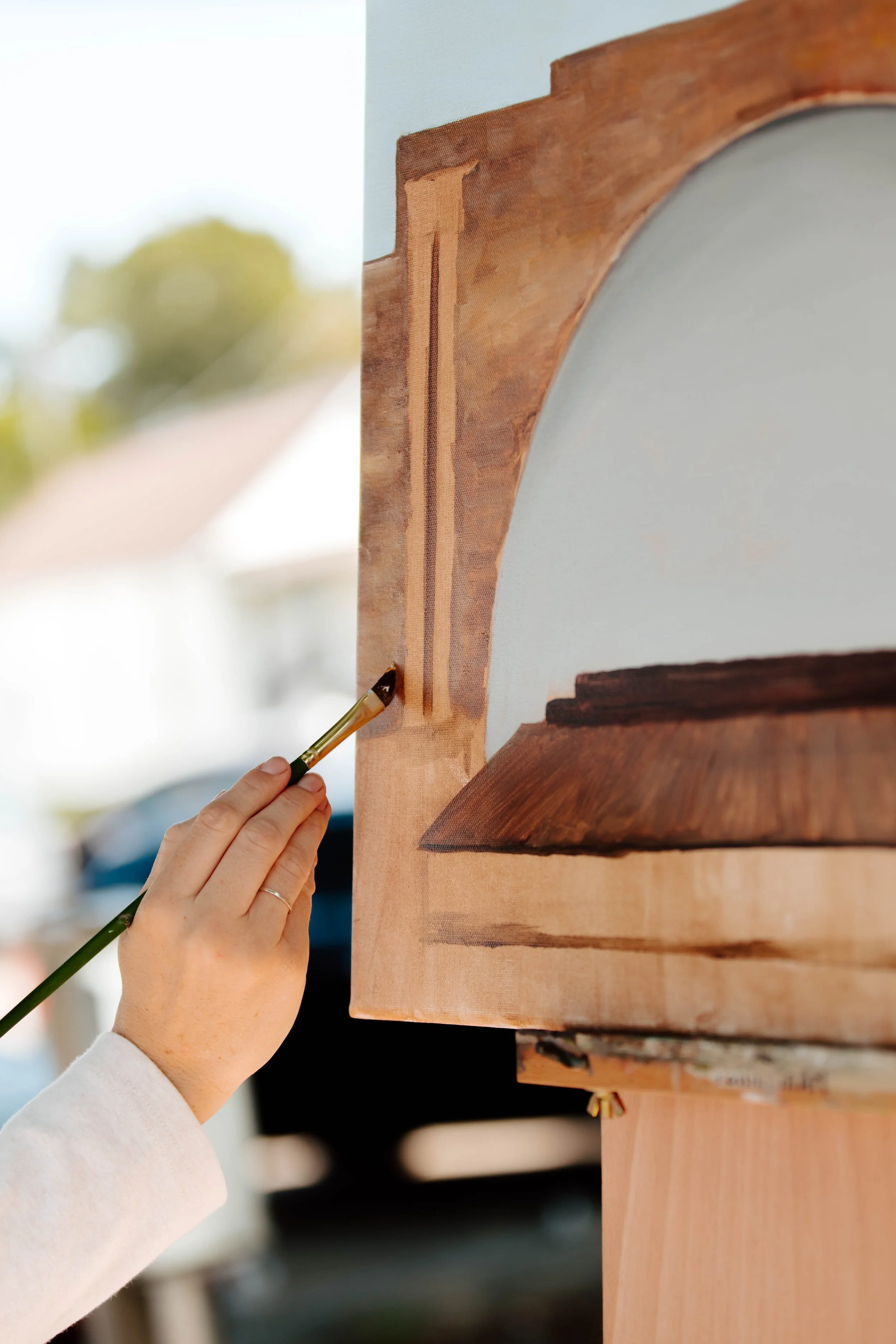 Image of an artist's hand painting on a canvas in plein air.