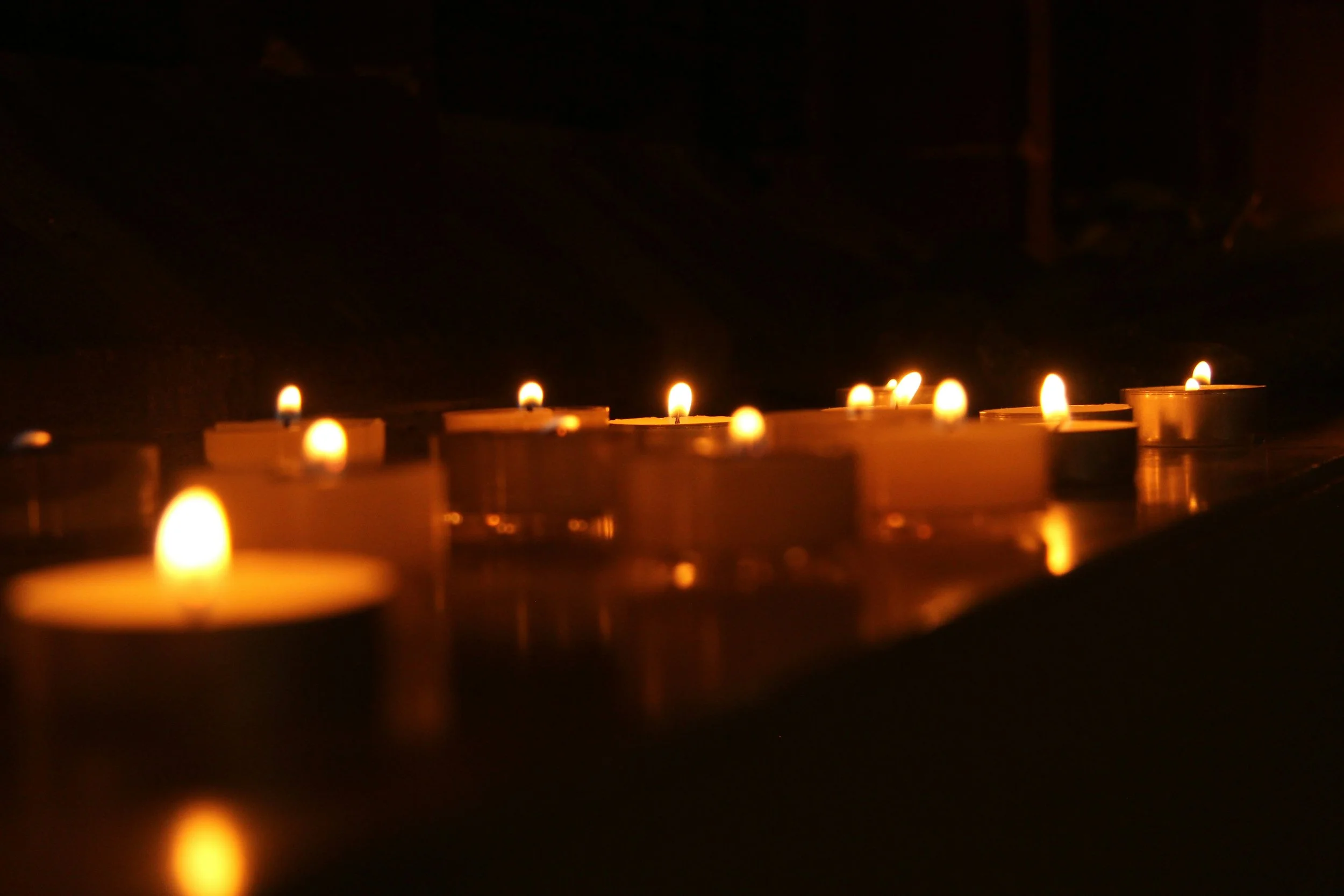 A row of small tea light candles burning in the darkness.