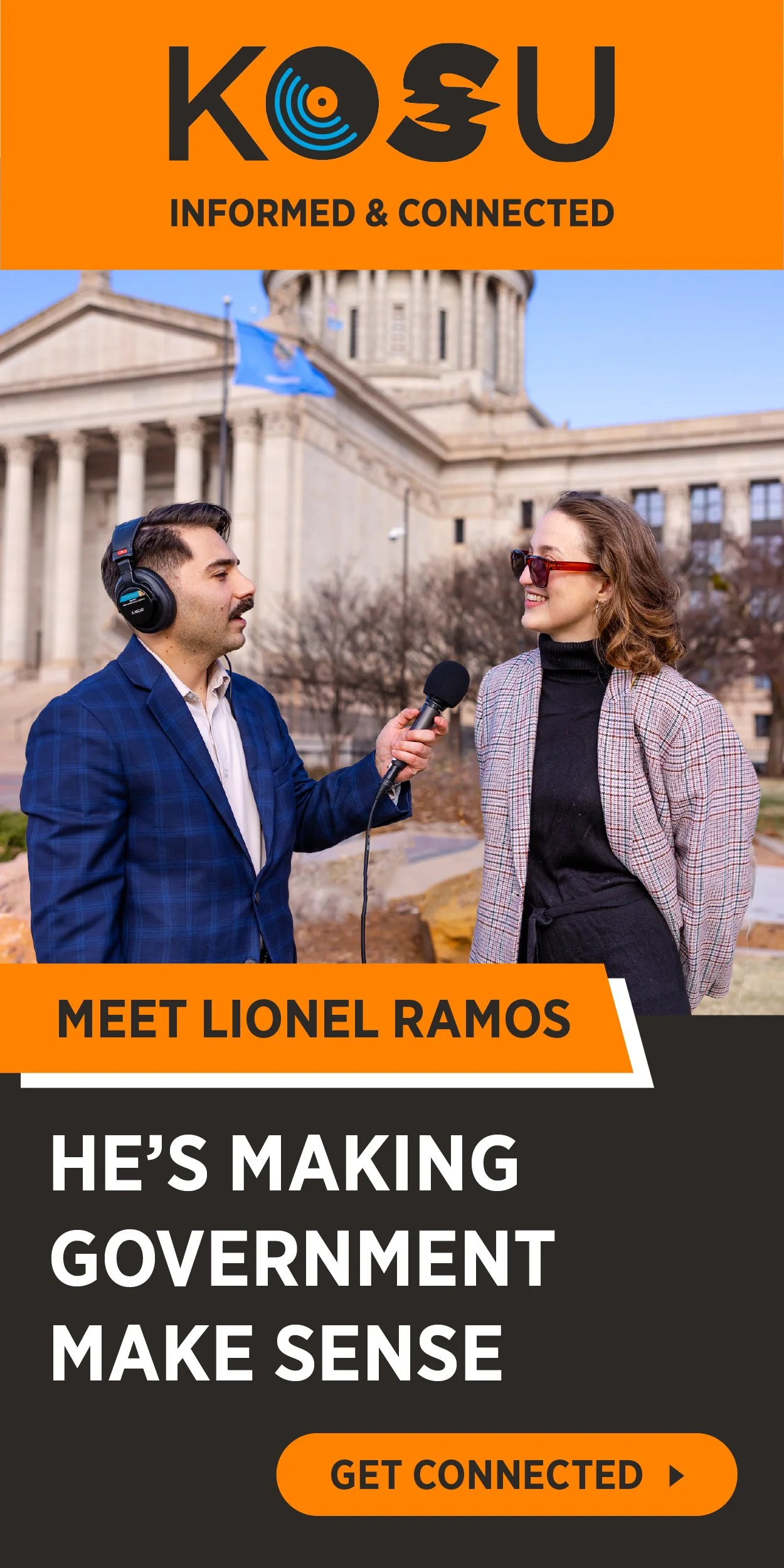 A man in a blue plaid suit interview a woman in a black turtleneck and plaid blazer outside a government building with columns, holding a microphone close to her. The background features a large domed government building and leafless trees.
