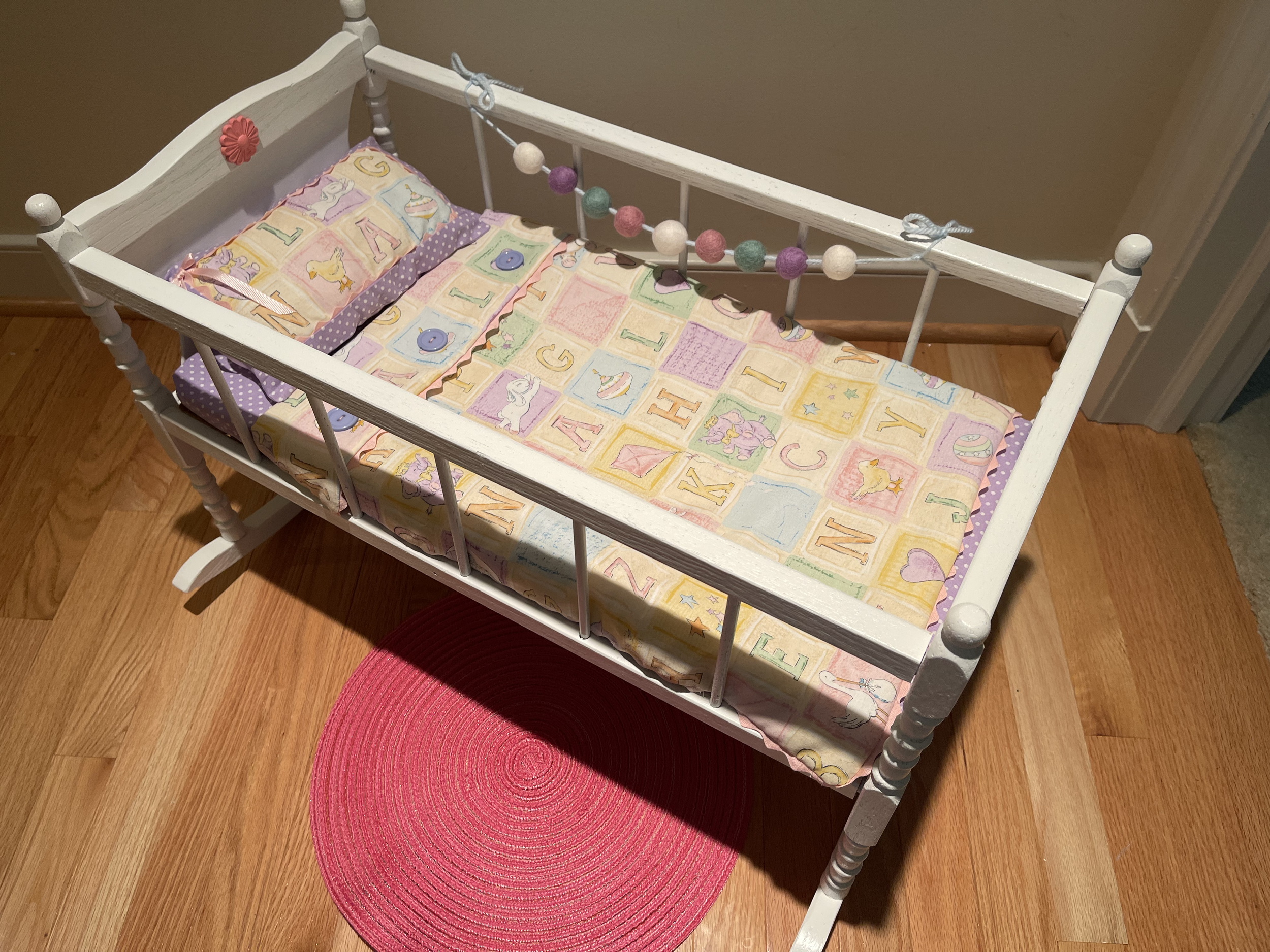 This wooden rocking crib features complete set of bedding and a garland along the side. $68