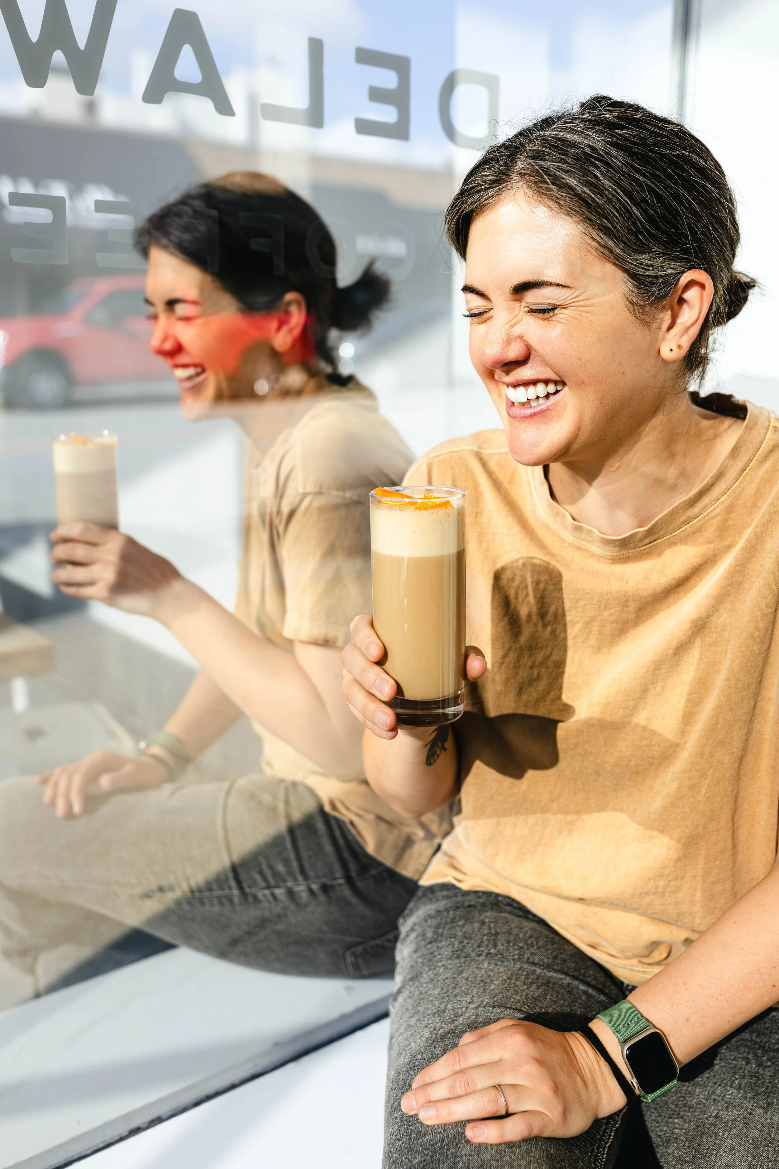 Woman laughing while holding a latte by the front window at Delaware Coffee Co.