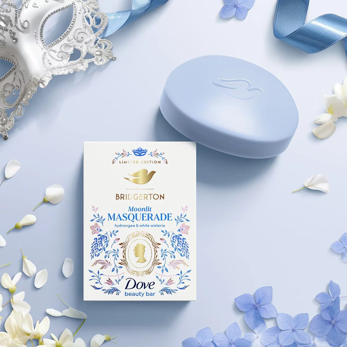 A Dove x Bridgerton beauty bar 'Moonlit Masquerade' with hydrangea and white wisteria flowers arranged around it, a blue decorative box with a dove logo on top, and a silver and blue masquerade mask in the corner. Illustrated by Maggie Enterrios