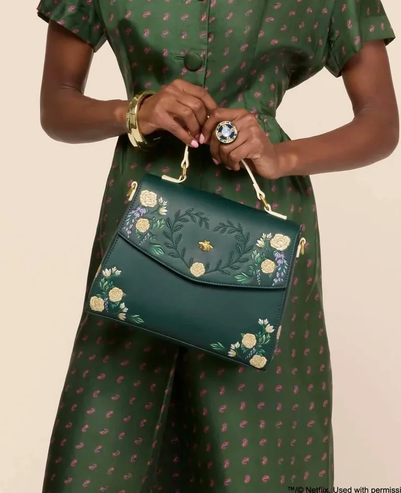 Pattern illustration by Maggie Enterrios for Bridgerton Loungefly limited edition collection. Image of green embroidered purse design held by woman in green dress