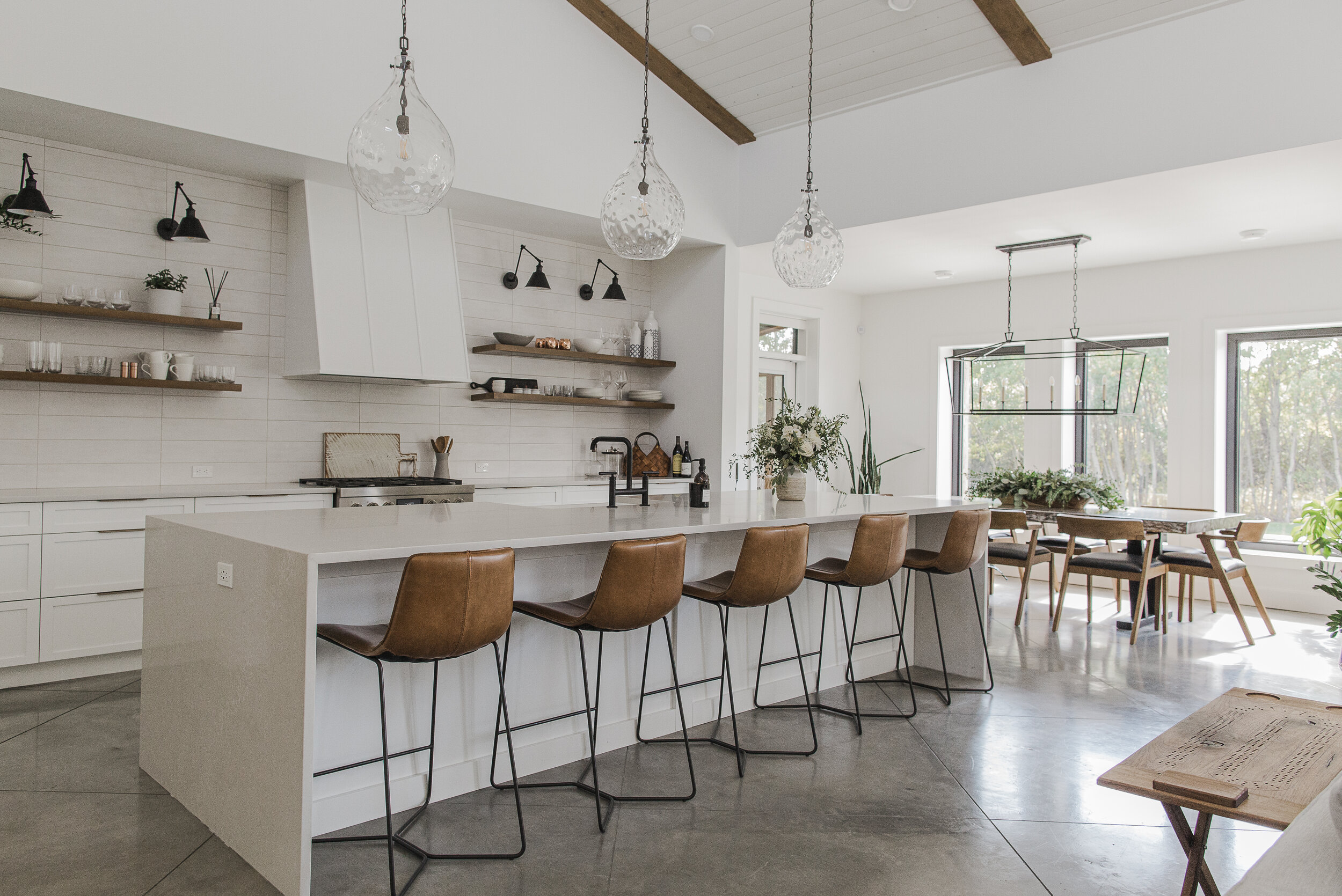 Modern custom kitchen interior built by Blackrock Homes & Commercial featuring large island, leather bar stools, pendant lights and dining area in a bright new home in Grande Prairie, Alberta