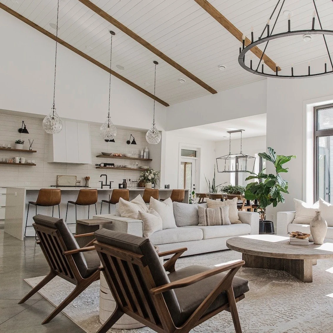 A vaulted shiplap ceiling, exposed beams, and an iron ring chandelier set the tone in this open great room. Walls of black-framed windows pull in the light, and the kitchen opens off the same space. Let's design something built around you &mdash; bla