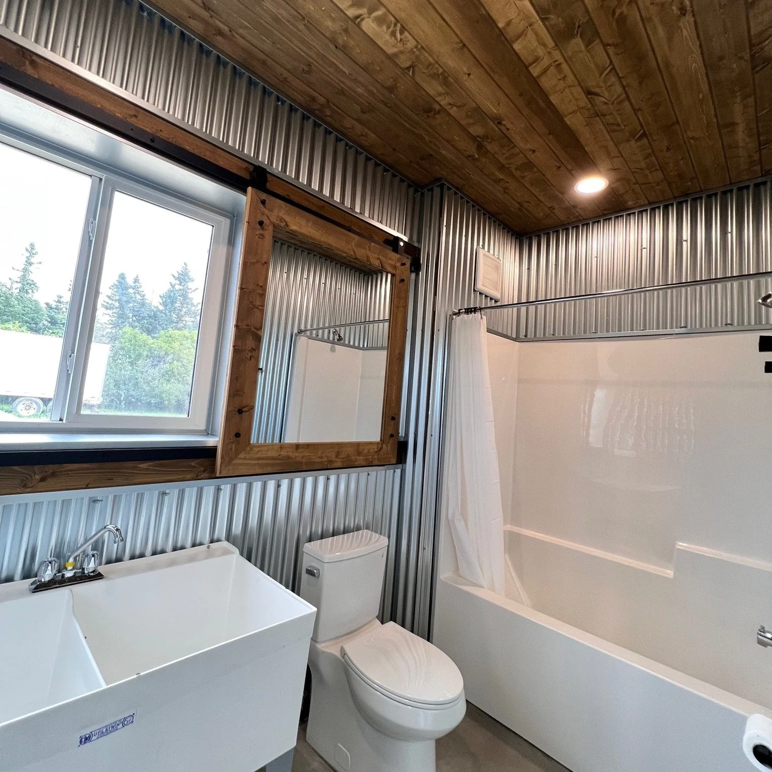 Staying with the Grainery Theme...a view when you want it &mdash; slide the barn-door mirror aside and the window does the rest. Corrugated steel, a warm pine ceiling, and polished concrete underfoot, character built into even the shop bathroom. Brin