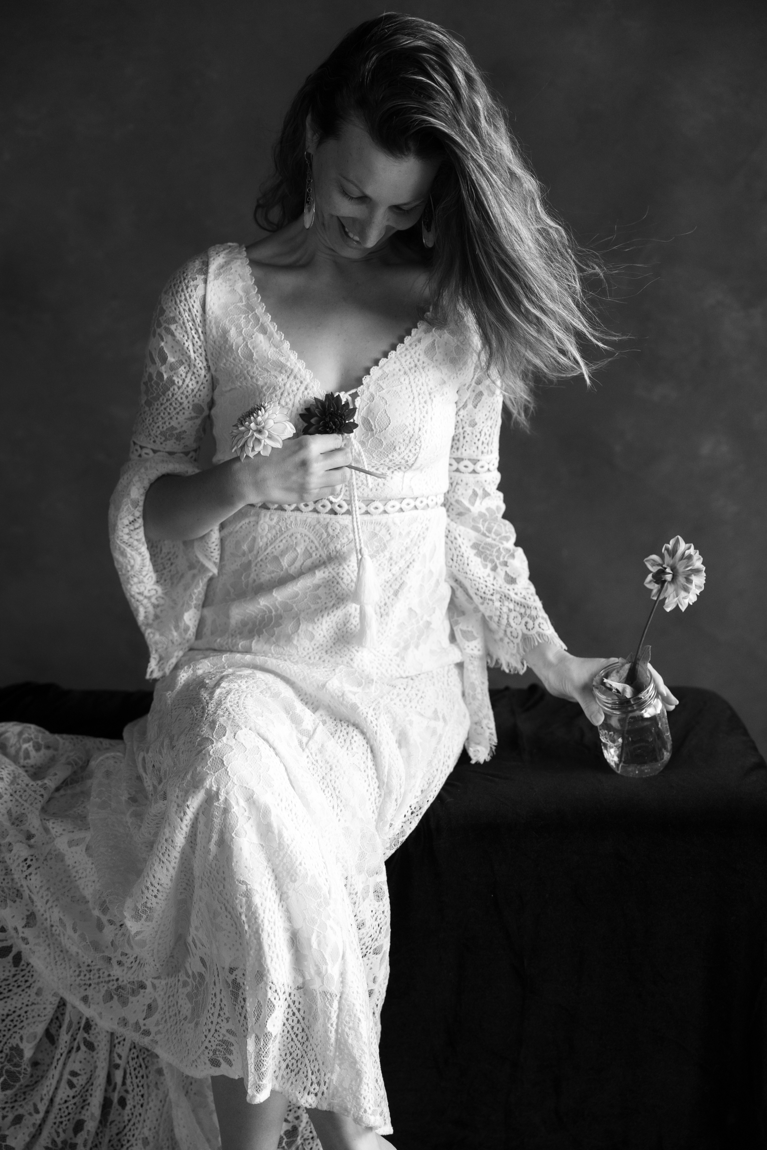 Authentic self-expression captured in a black and white portrait of a woman smiling in a white dress with flowers during a Just BE self-love session near Pismo Beach CA.