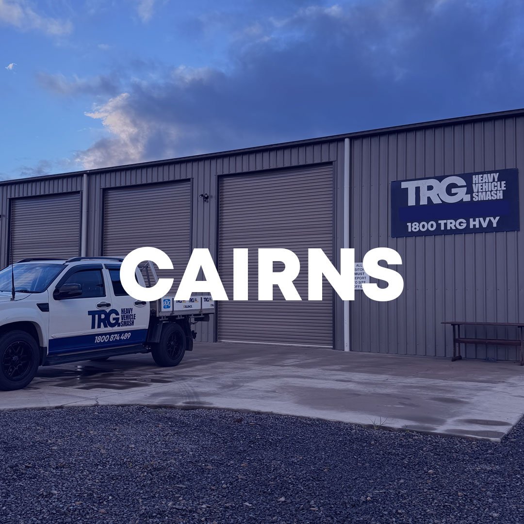 Exterior view of a truck repair facility with trucks and vehicles parked outside, large signage displaying TRG Truck Repair Group, blue sky with clouds, and 'CAIRNS' text overlayed at the top.