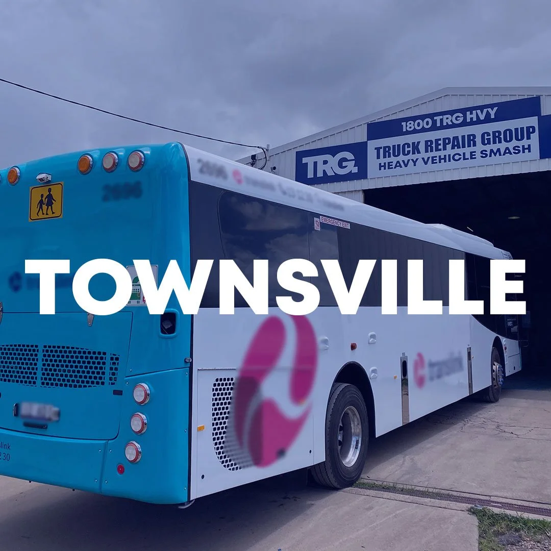 Outdoor view of a bus depot in Townsville, featuring a parked white bus with "Sunbus" branding next to a chain-link fence. In the background, a building labeled "TRG Truck Repair Group" is visible under a clear blue sky.