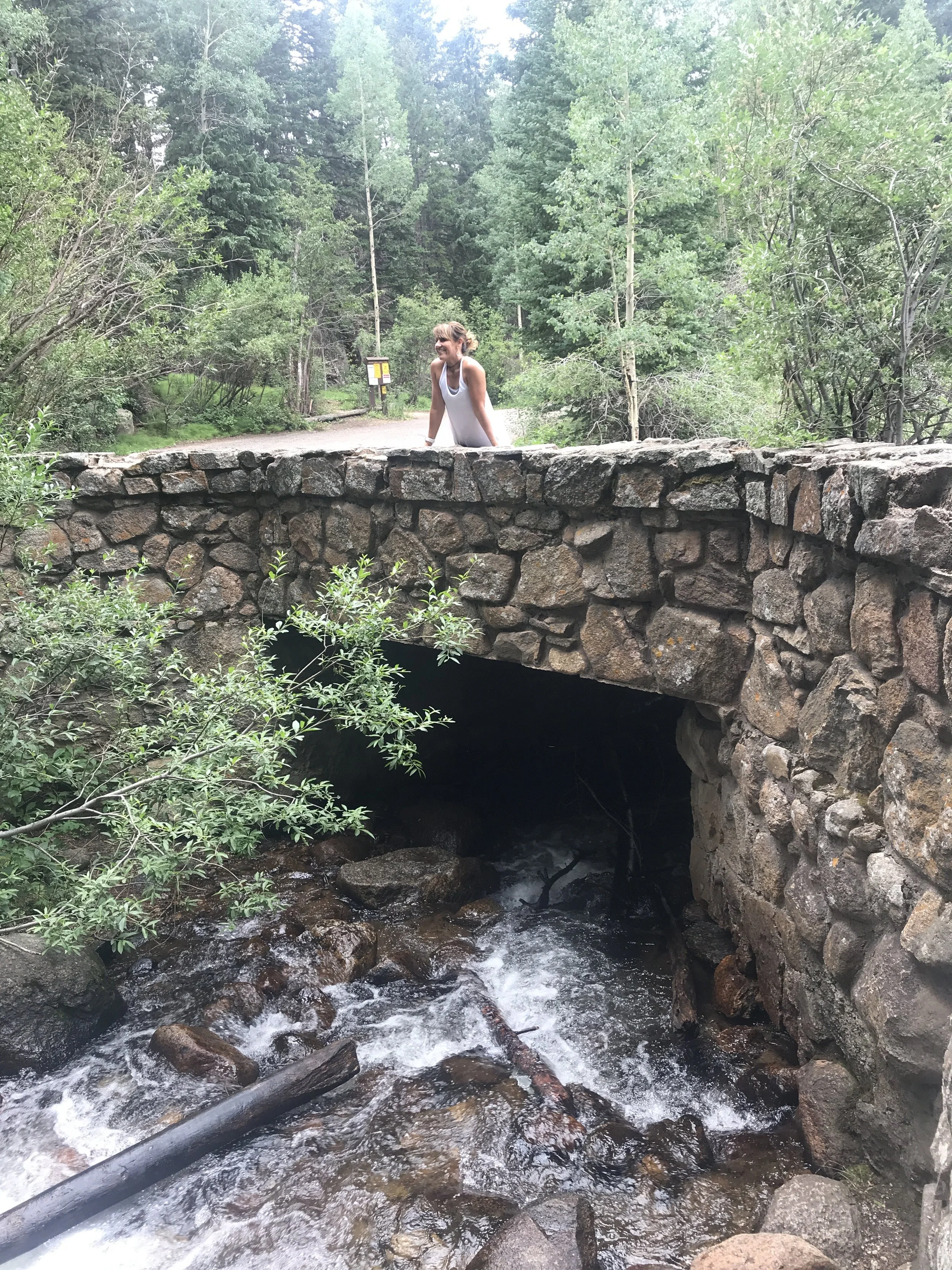 a woman standing on the top of a stone bridge with a river flowing under