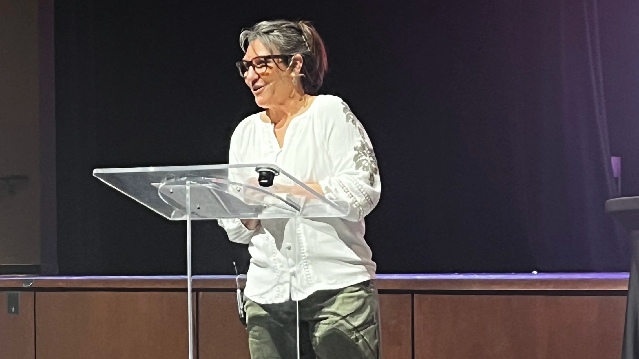 a woman standing at a podium with a smile sharing her story