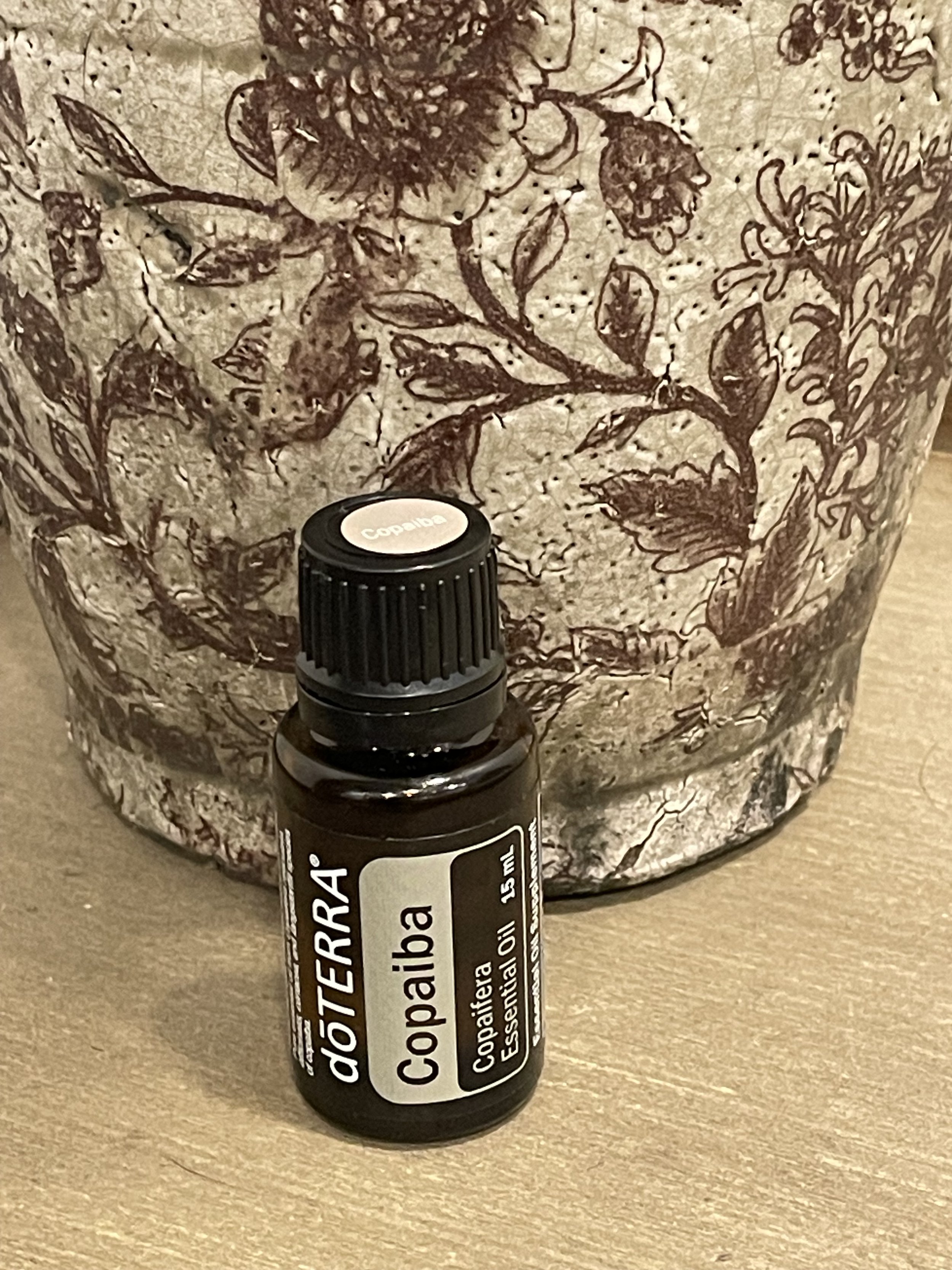 bottle of doTERRA Copaiba essential oil by a brown flower vase