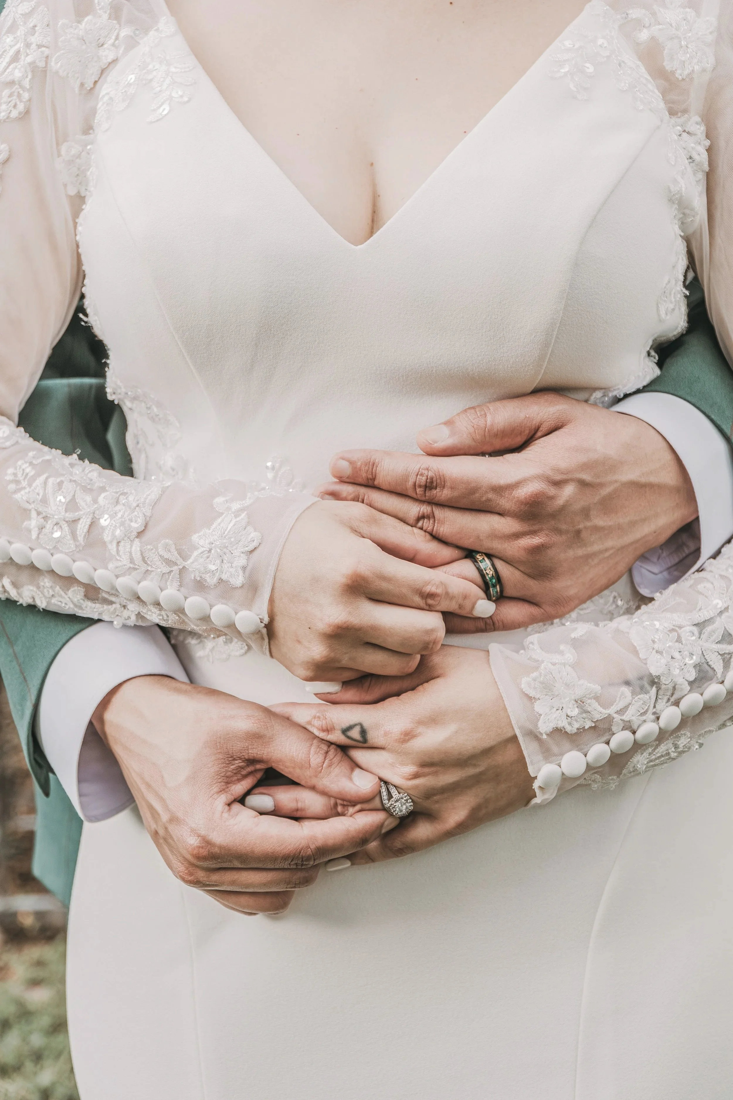 Close-up of a couple in wedding attire, with the bride wearing a white lace dress and the groom wearing a green suit, embracing and holding hands.