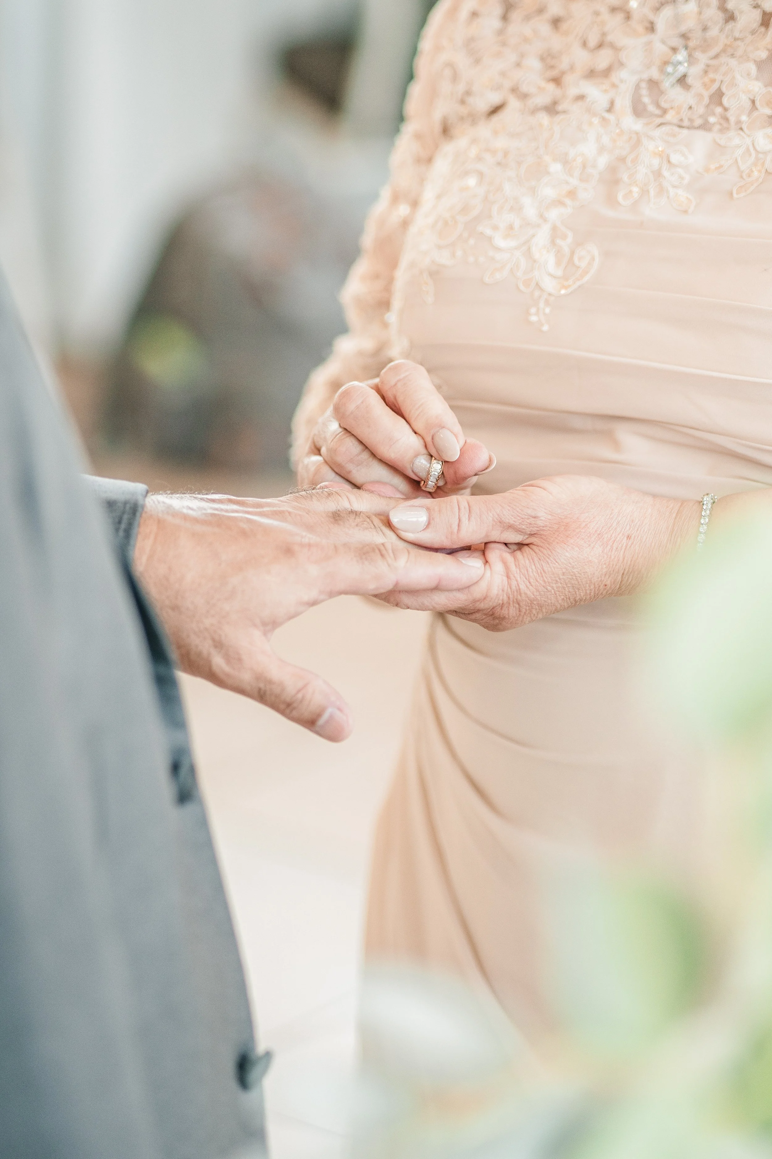 Close-up of a wedding ceremony where a woman is placing a ring on a man's finger, focusing on their hands and rings with a softly blurred background.
