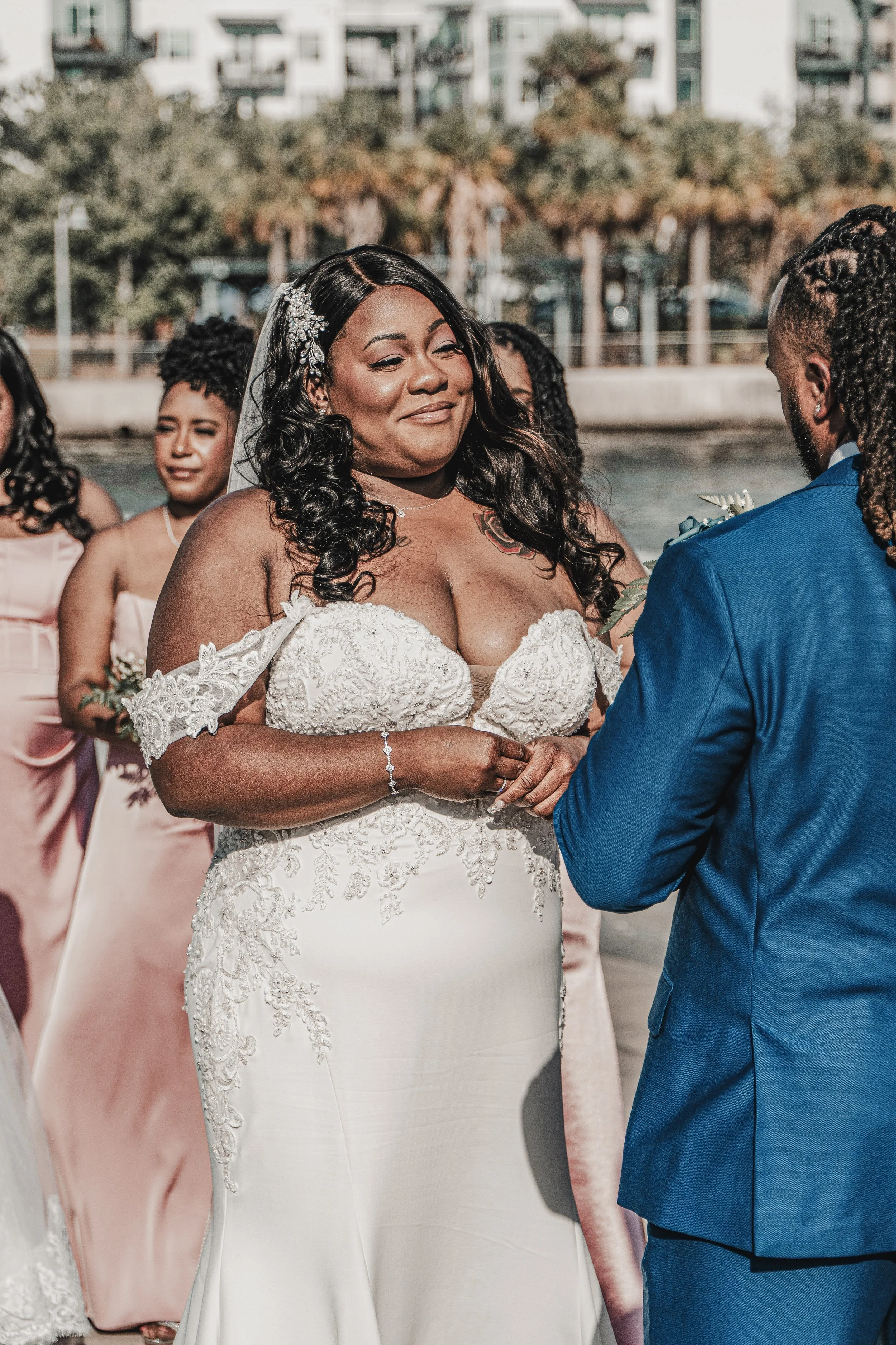 A bride and groom exchanging vows at their outdoor wedding ceremony, with bridesmaids in pink dresses in the background.