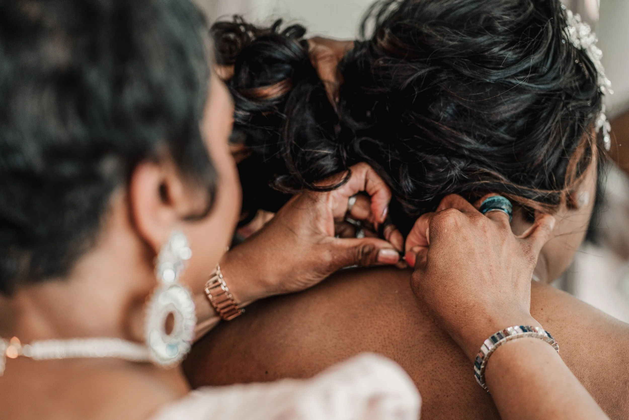 Close-up of hands adjusting a woman's hair at her wedding or special event, with focus on her dark, curly hair and jewelry.