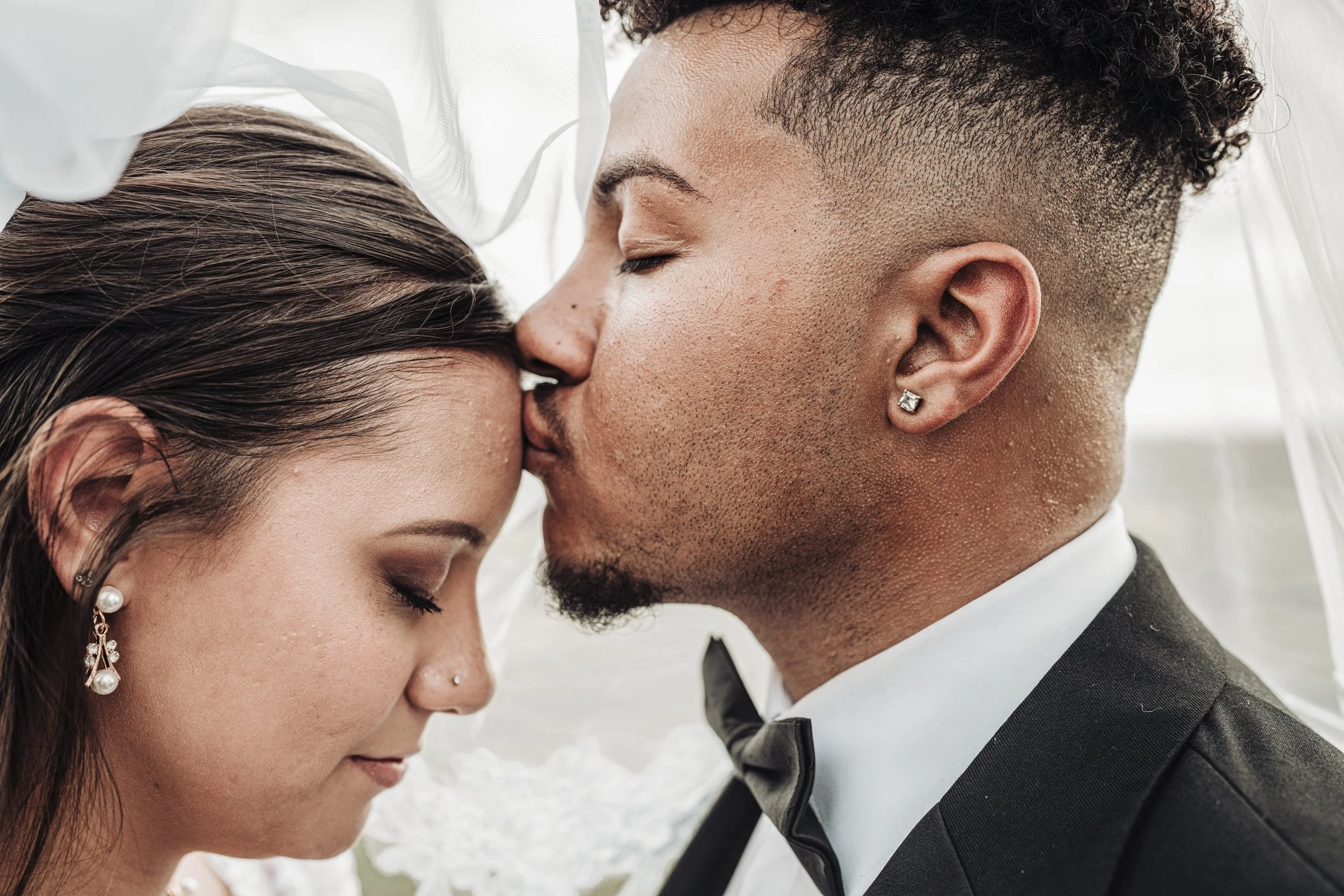 A close-up of a bride and groom sharing a kiss during their wedding, with their foreheads touching and eyes closed, dressed in wedding attire.