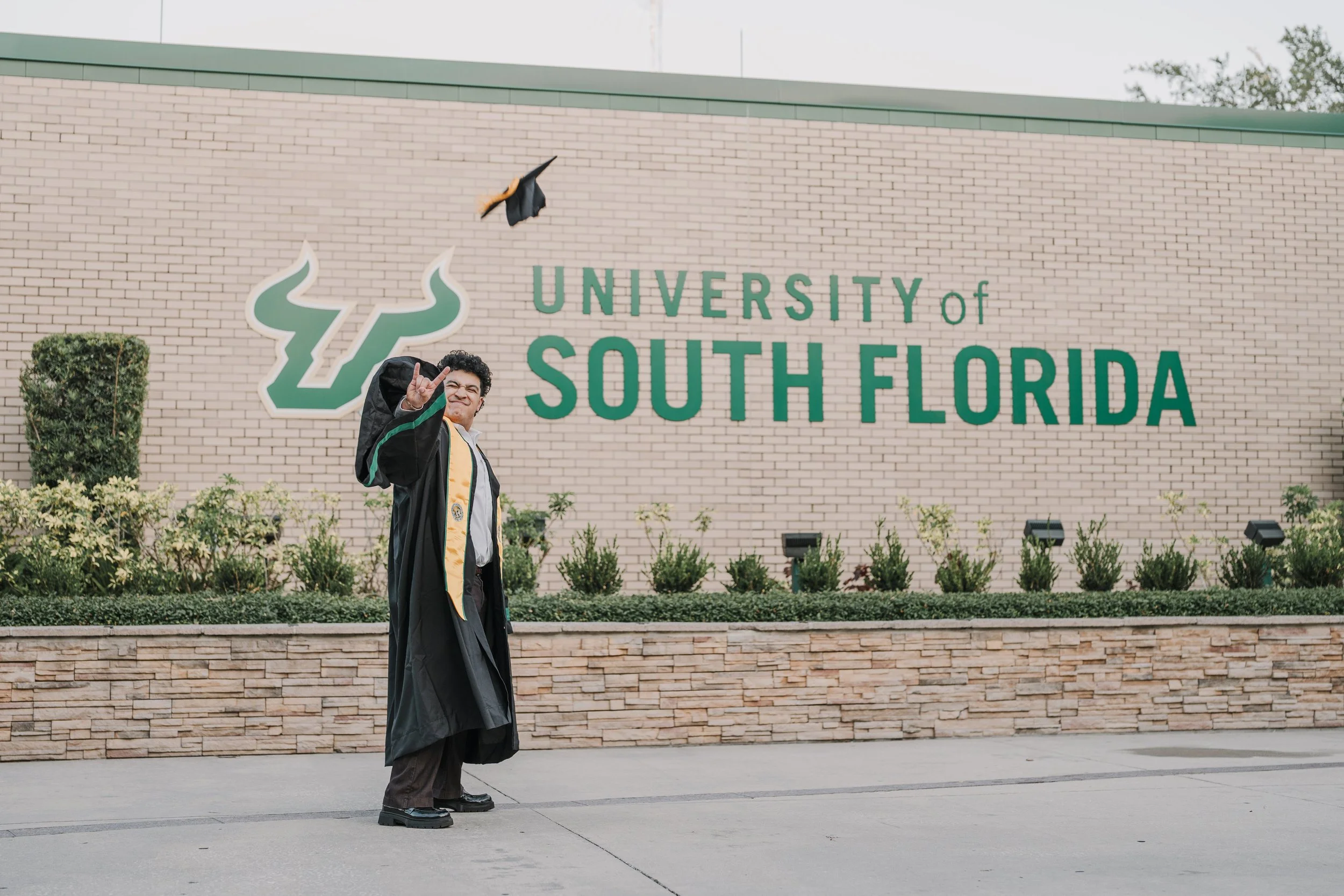 Graduate throwing cap in front of University of South Florida sign.