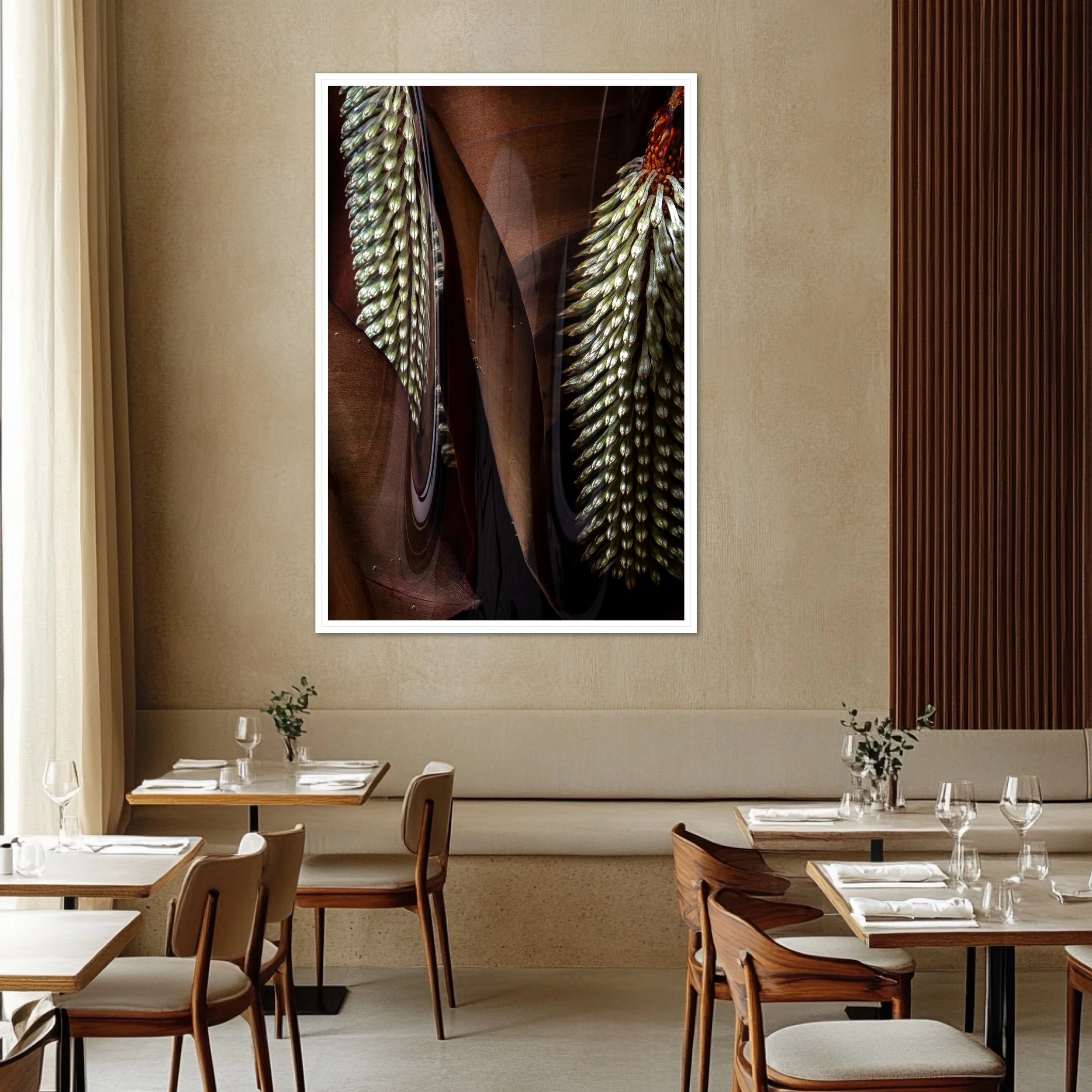 A restaurant interior with wooden tables set with white napkins and glassware, decorated with small green plants, facing a beige wall with a large framed artwork of a close-up of a plant.