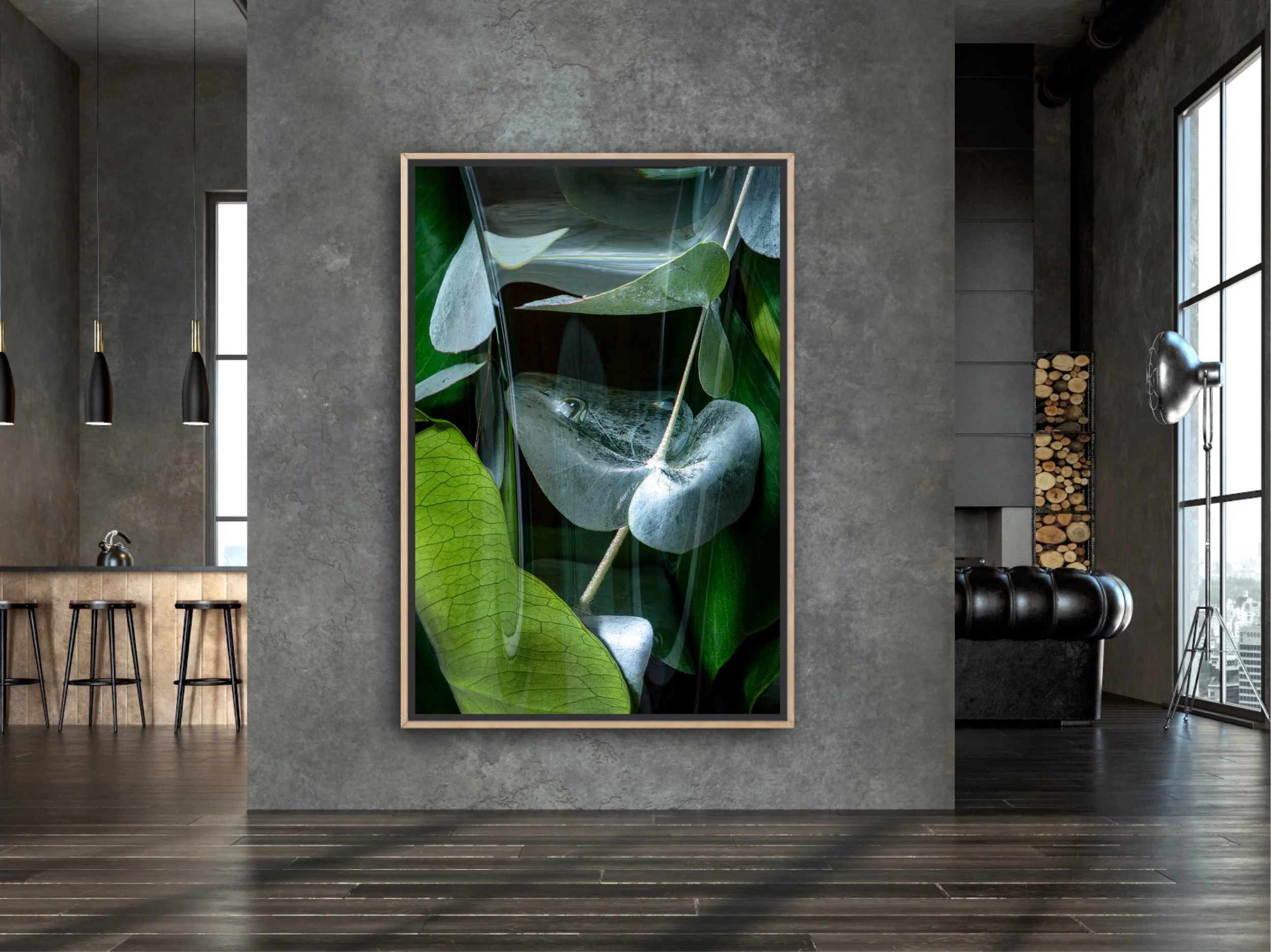 Interior of a modern room with concrete walls, dark wood flooring, and large windows. A large framed artwork of green leaves hangs on the wall, with a kitchen island and barstools visible on the left, and a sitting area with a black leather sofa, woo