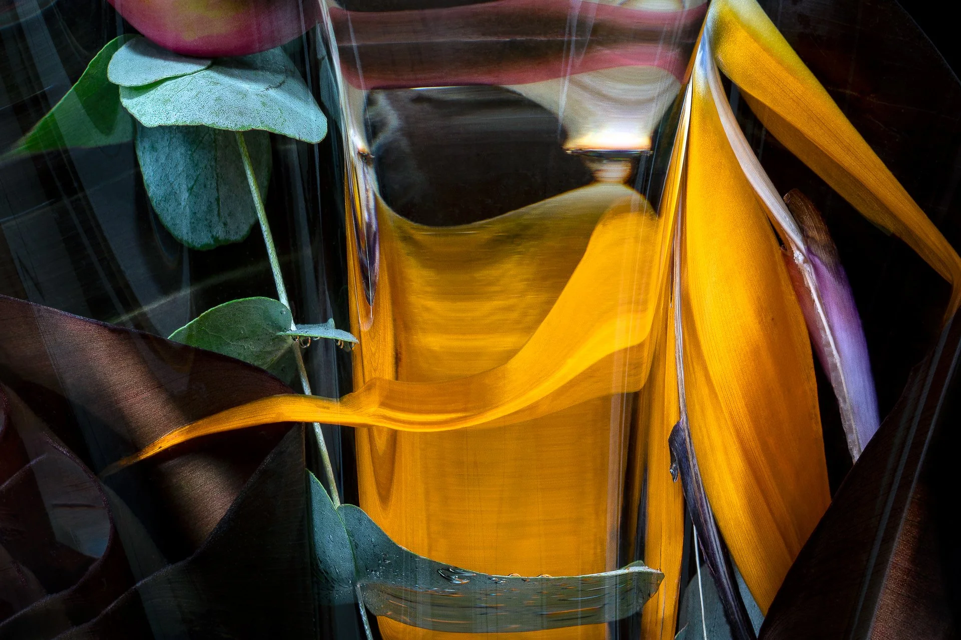 Close-up of abstract glass artwork with green leaves in the background and yellow and black streaks in the foreground.