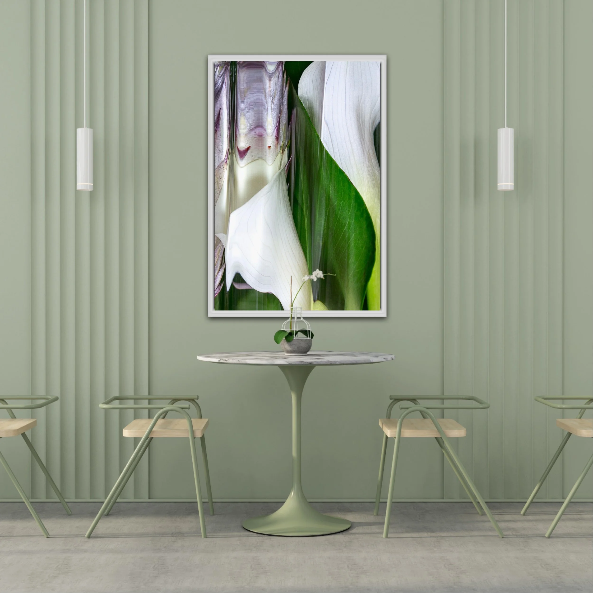 Interior scene with green walls, a white round table, benches with light wood seats and metal legs, two hanging pendant lights, and a framed botanical photograph of white calla lilies and green leaves.