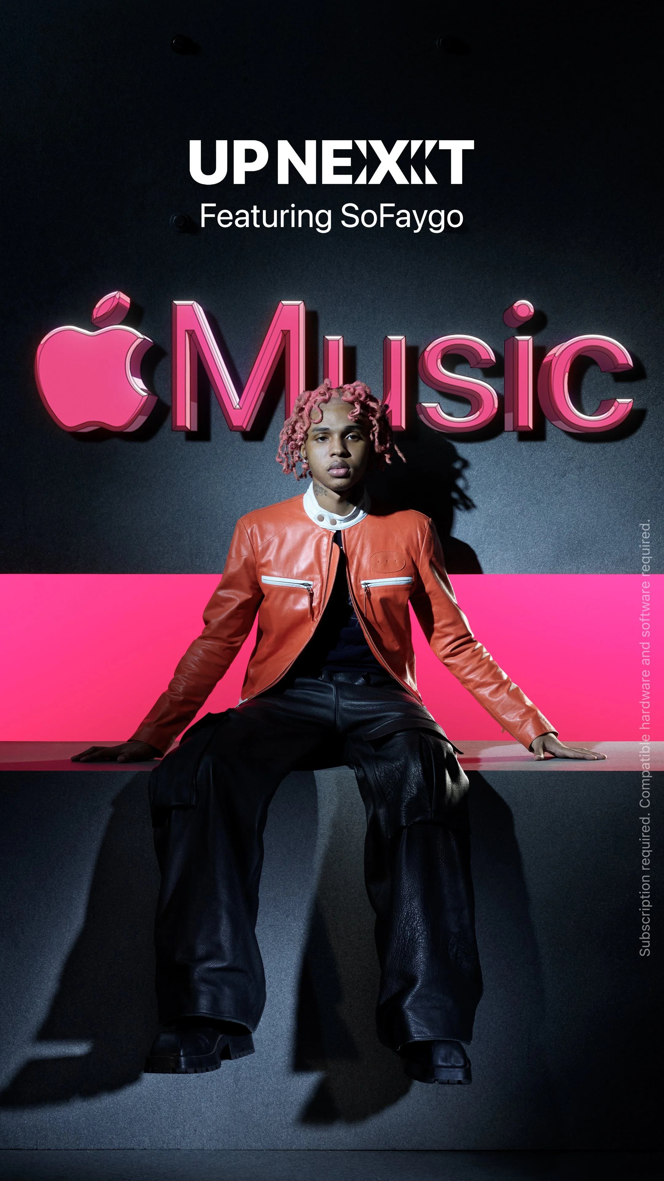 A person with pink dreadlocks wearing a red leather jacket and black cargo pants sitting on a black platform in front of a sign that says 'UPNEXXT Featuring SoFaygo' with a pink Apple logo and the word 'Music' in pink 3D letters.