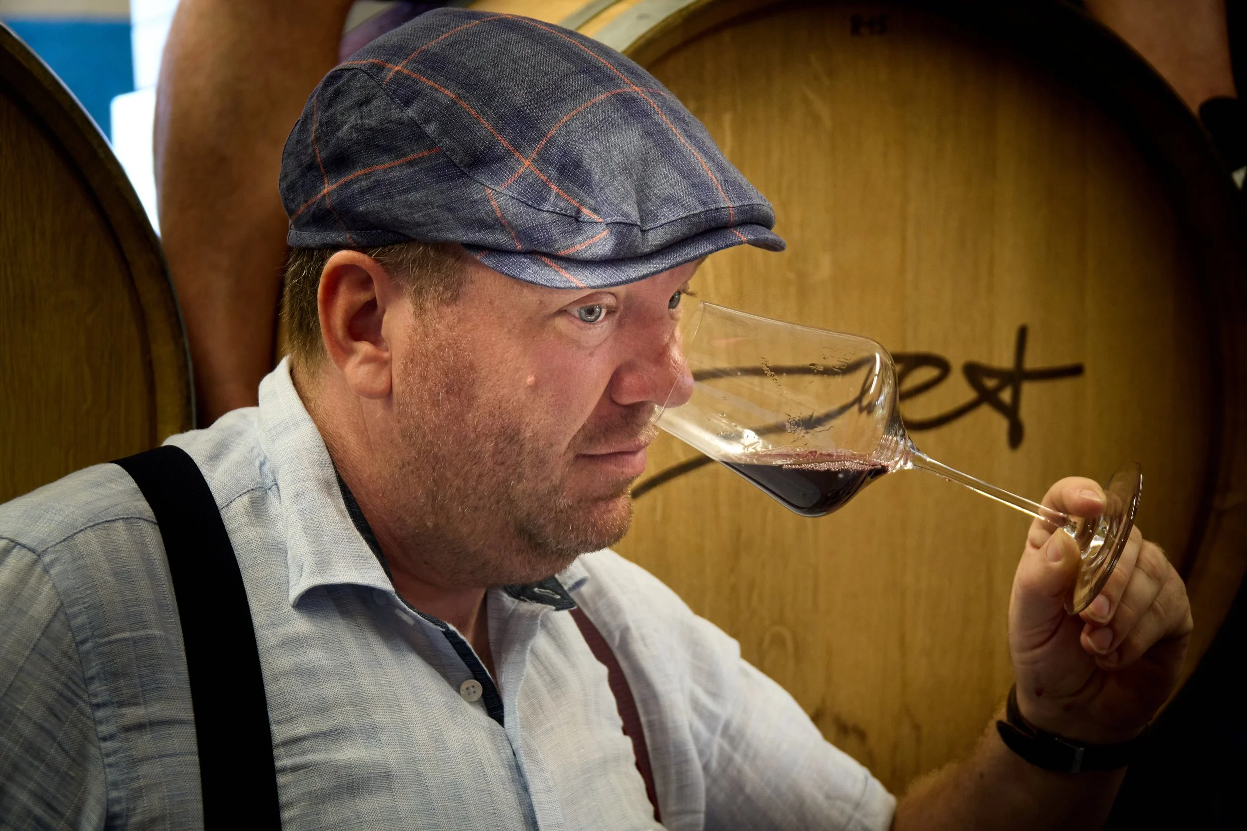 Mann mit grauem und rotem Karo-Hut, trinkt Rotwein aus einem Weinglas